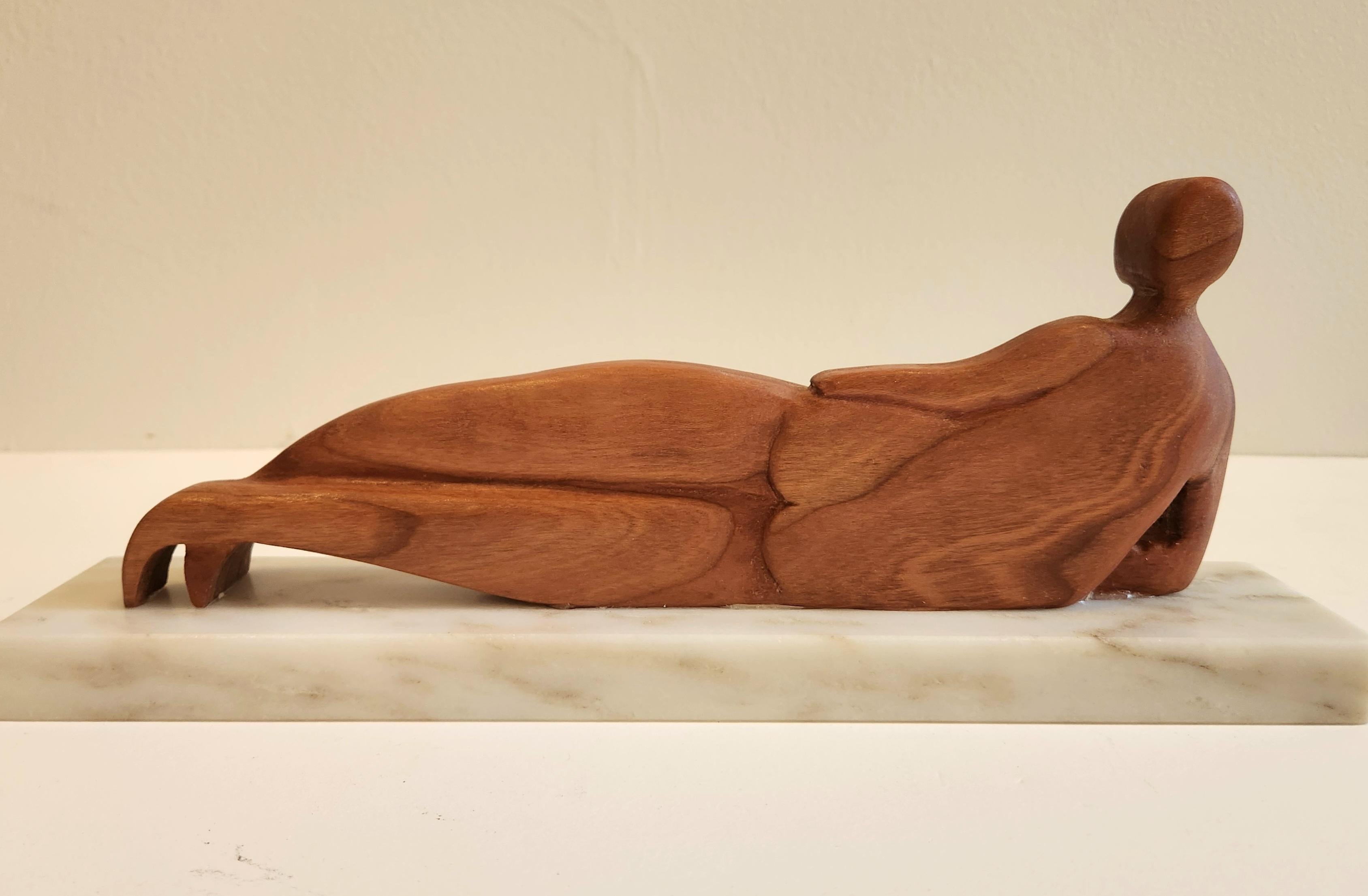 Questa bellissima scultura in legno di ciliegio su una base di marmo mostra la figura di una donna reclinata. Il corpo della donna è stilizzato, con un'enfasi sulle curve e sul flusso del corpo. Le sue gambe sono intrecciate con grazia alle