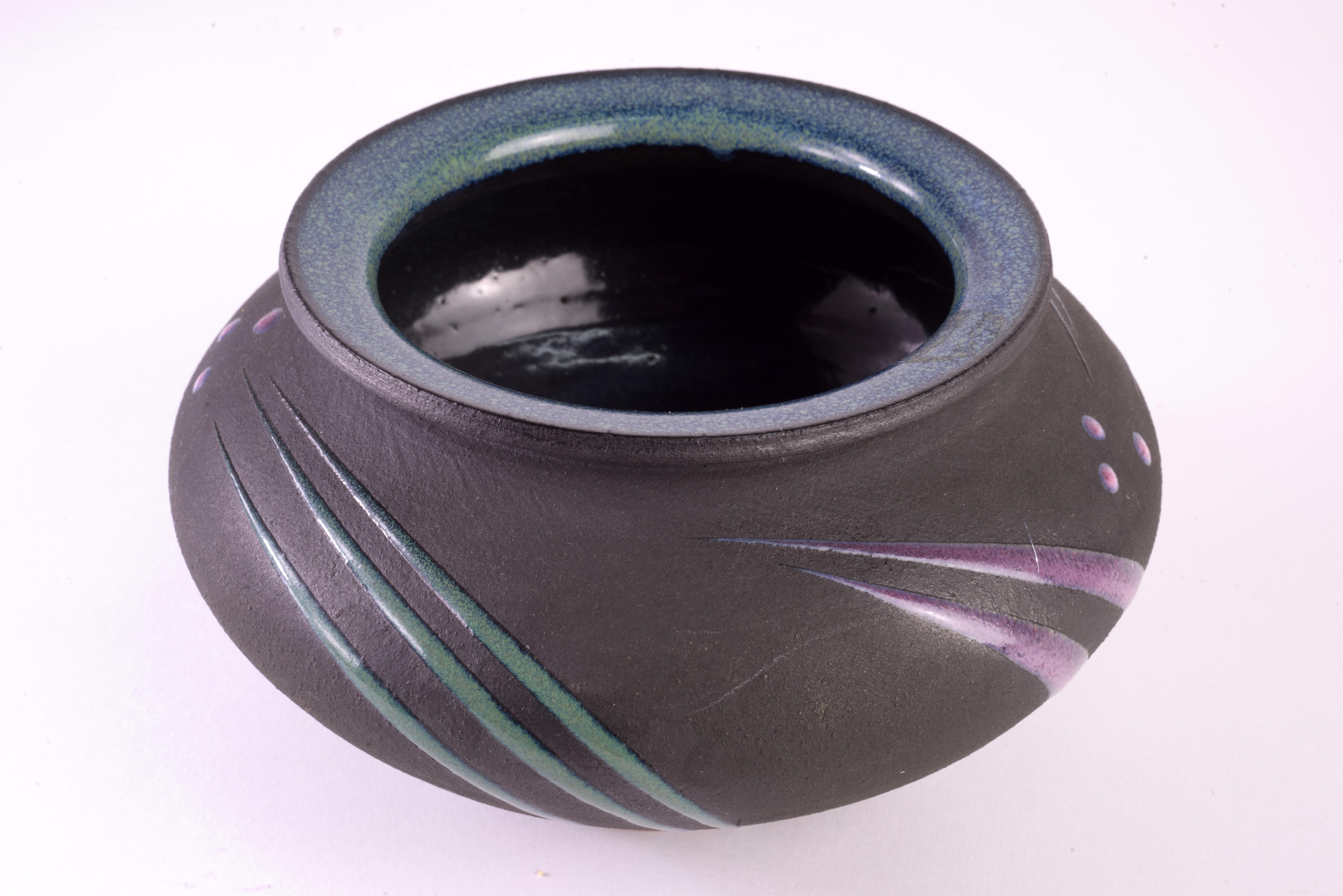 ostmodern bulbous ceramic vase was hand thrown and hand decorated by Michael Cho with black matte finish and raised pink and green abstract geometric decorations done in glossy glaze. The rim and interior are also glazed in glossy mottled green