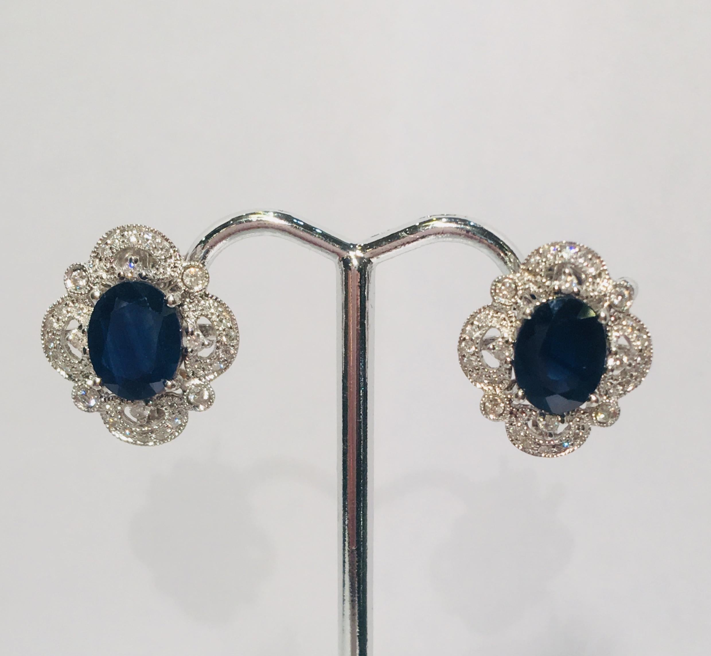 Elegant 14 karat white gold post earrings for pierced ears from noted Beverly Hills jeweler, Michael Christoff, feature a prong set, oval cut, dark blue sapphire surrounded by a sparkling filigree halo of bezel, prong and pave set diamonds, giving