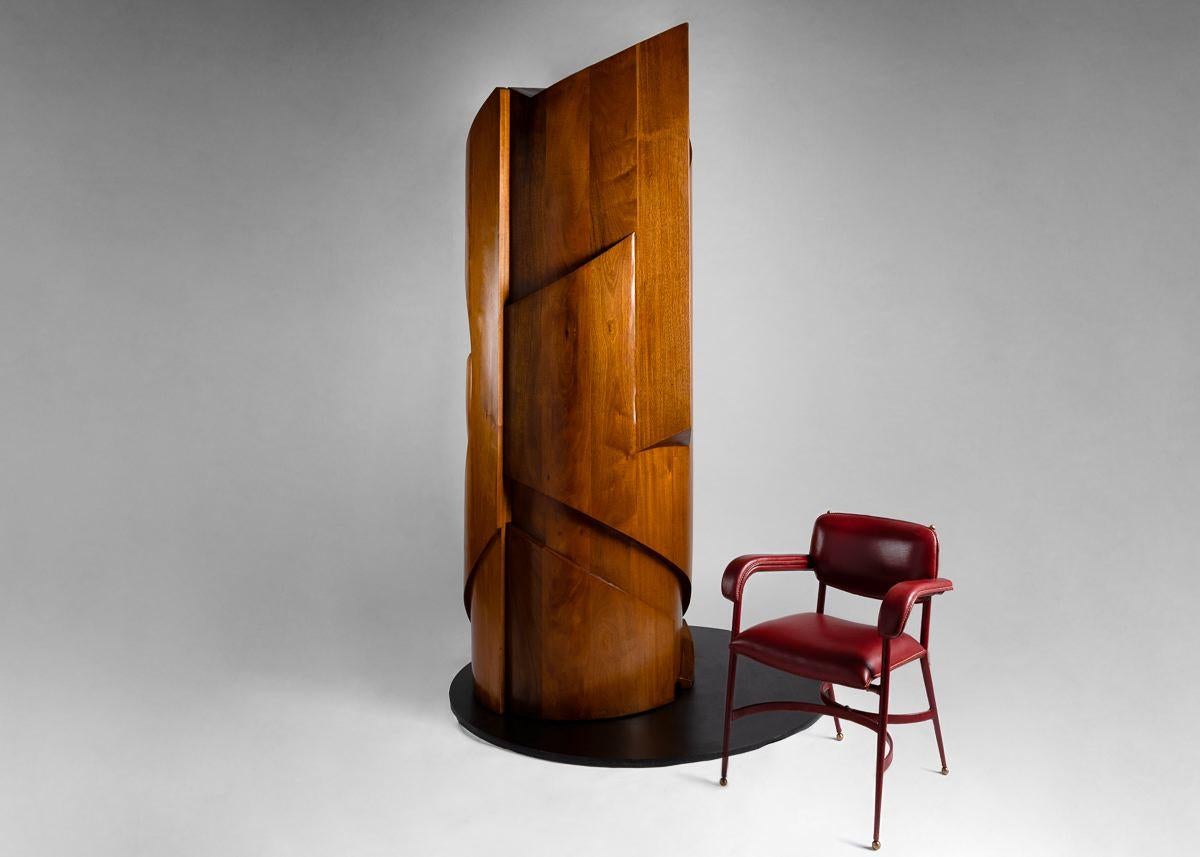 This sculptural cabinet is carved from solid, 4-inch thick Mahogany, and weighs 900 lbs. It is divided in two halves. One half is a door, which swings out on hidden hinges and concealed casters. The other half contains revolving shelves and drawers.