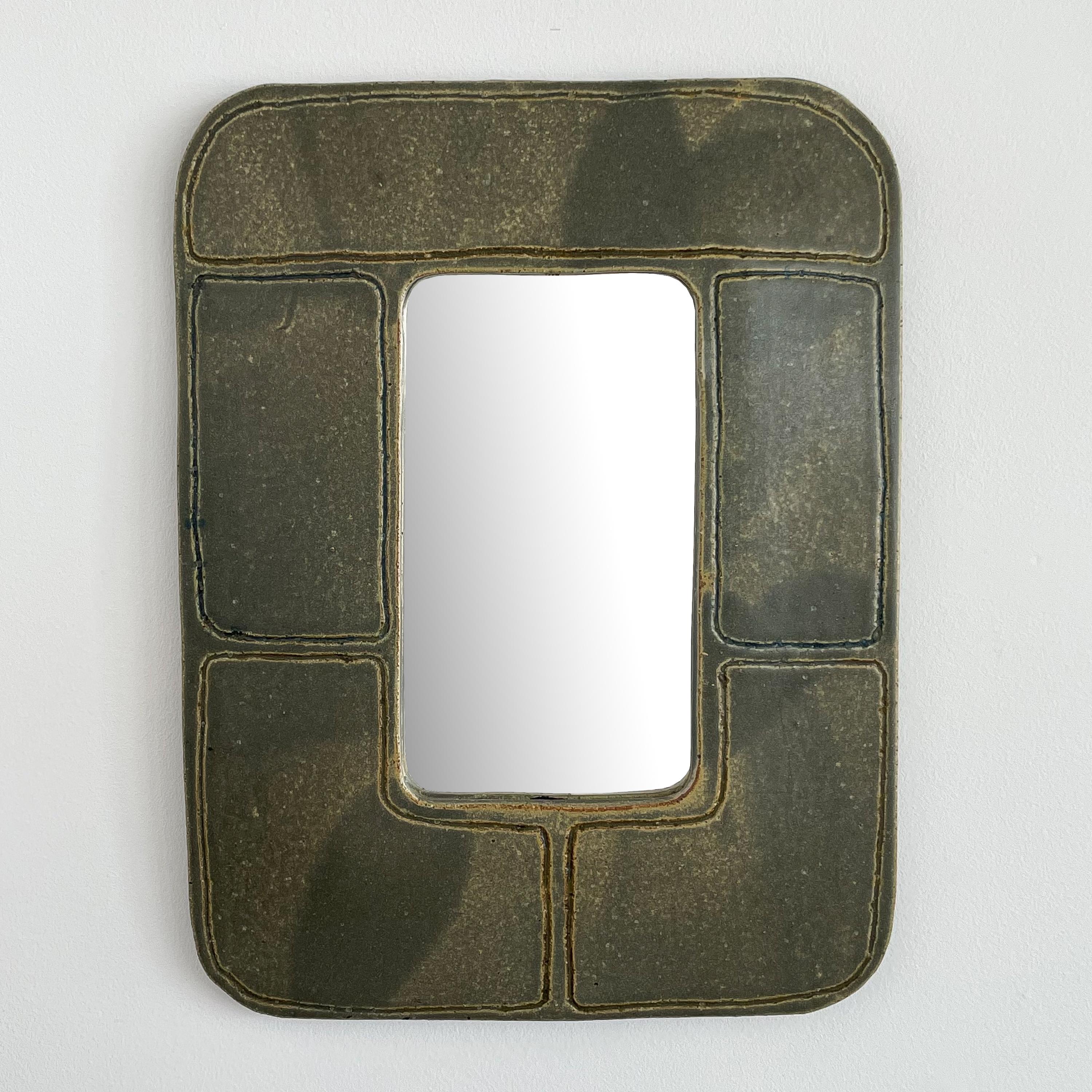 A 1960s stoneware pottery mirror by Massachusetts potter, Michael Cohen. This mirror features a hand built slab style frame with green glaze and incised minimalist geometric design. Signed with the Cohen mark and signature to the back. Cork covers