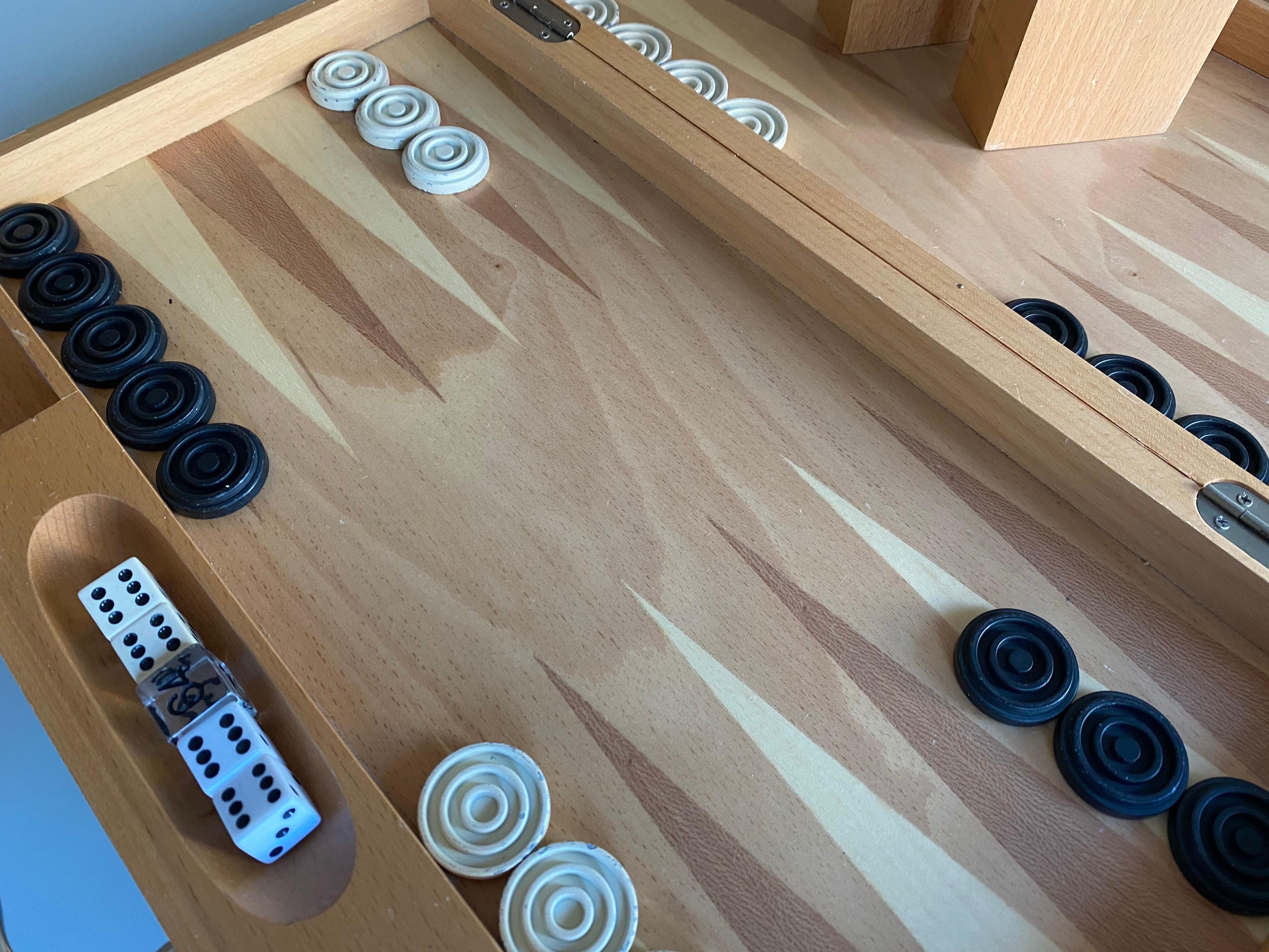 A Michael Graves designed backgammon board in light beech wood.

Set includes thirty heavy cast metal pieces in cream and black, two pair of dice, doubling cube, and dice cups in matching wood.

Case measures 17.25