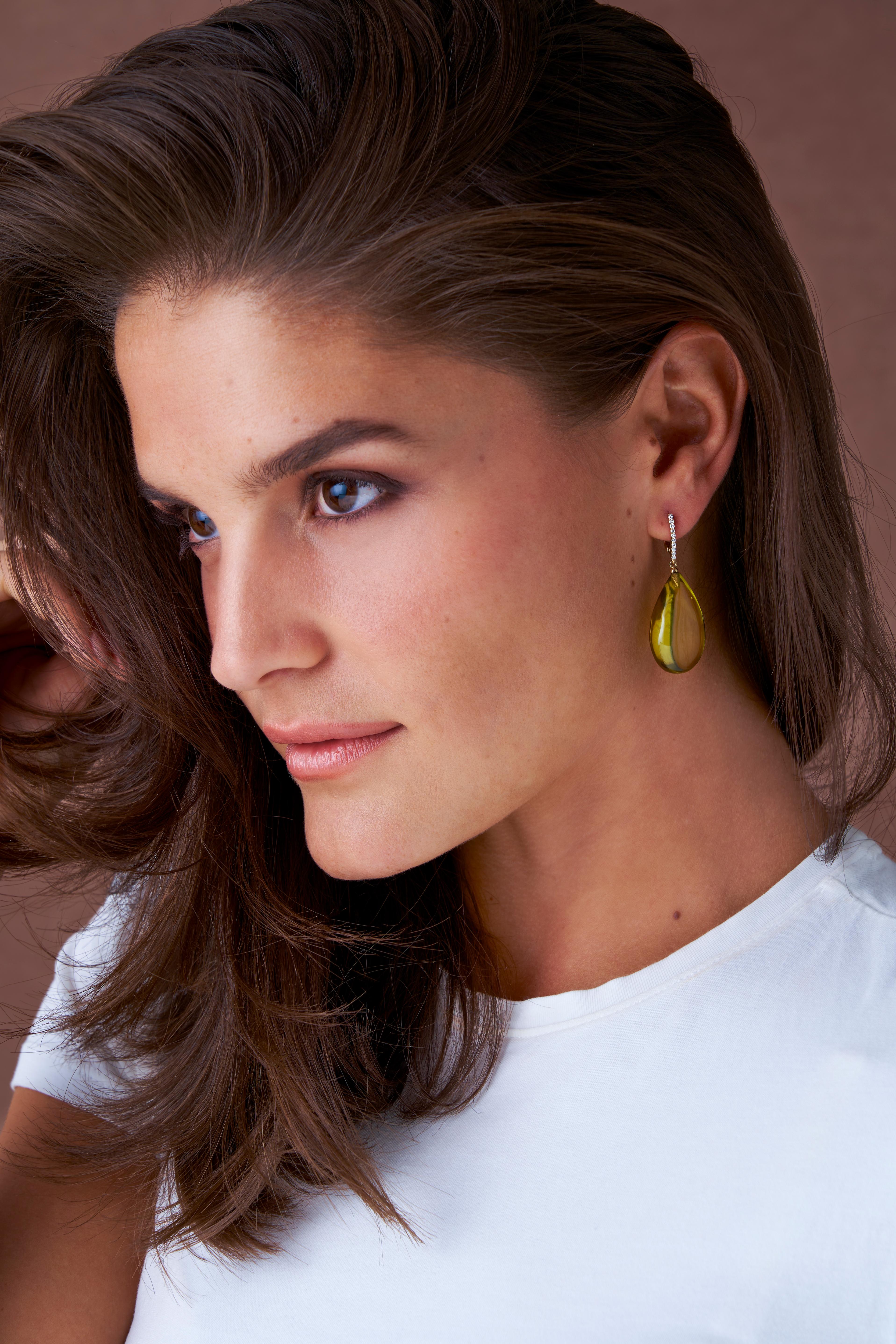 Stunning smooth green amber drop earrings, adorned with exquisite diamonds and crafted in luxurious gold.  The warm tone of the green amber is simply mesmerizing, with the silky smooth surface adding a touch of sophistication to the organic design. 