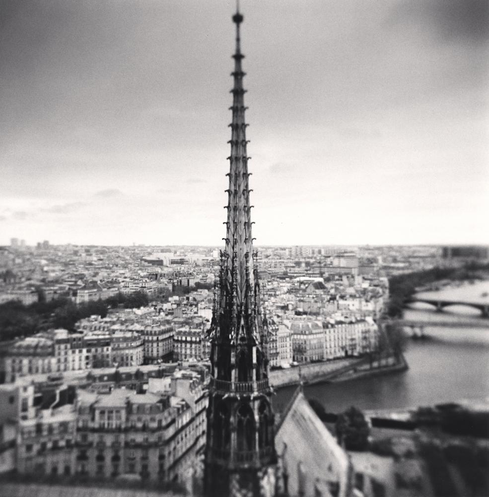 Spire, Notre Dame, Paris, France by Michael Kenna is a limited edition black and white photograph of the spire of the Notre Dame cathedral from an aerial view. The city of Paris and the Seine river can be seen in the distance. 

Image size: 8 x 7.75