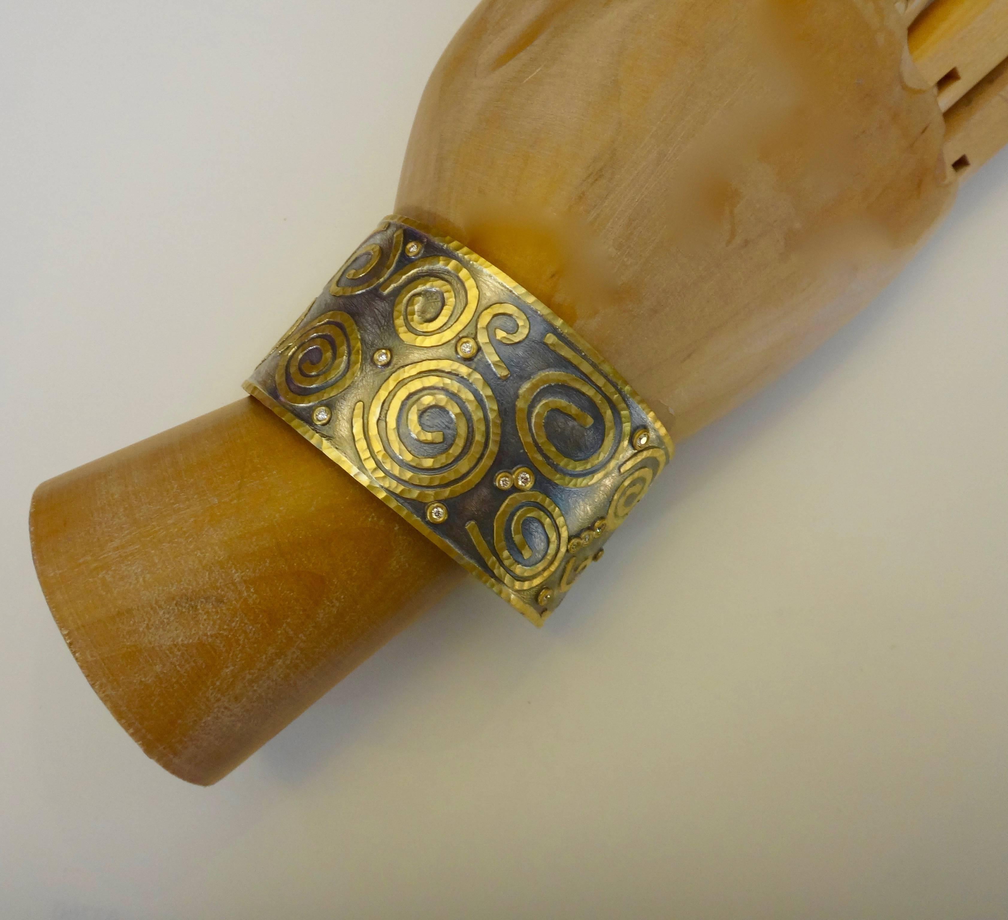 A composition of 24k gold spirals and bezel set white diamonds comprise this cuff bracelet.  The design elements are mounted on a textured and blackened sterling silver base.  This bracelet would look great with Michael Kneebone's 