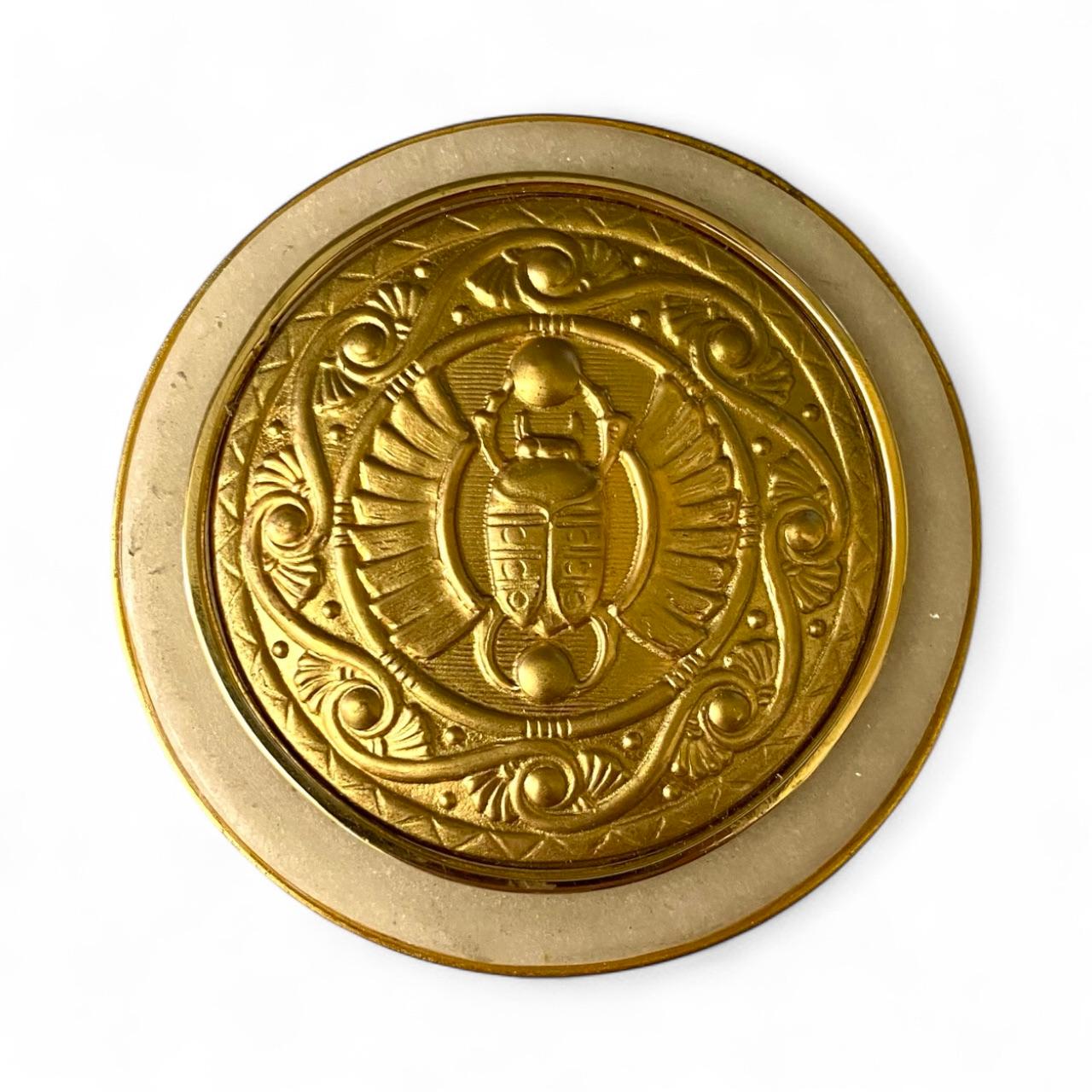 Alabaster forms the foundation for this elegant Egyptian influenced ring box.  Mounted on the top is a gilt bronze plaque featuring a scarab beetle with a scrolled frame.  The plaque is enclosed in gold.  Gilt bronze rims encase winged scarabs