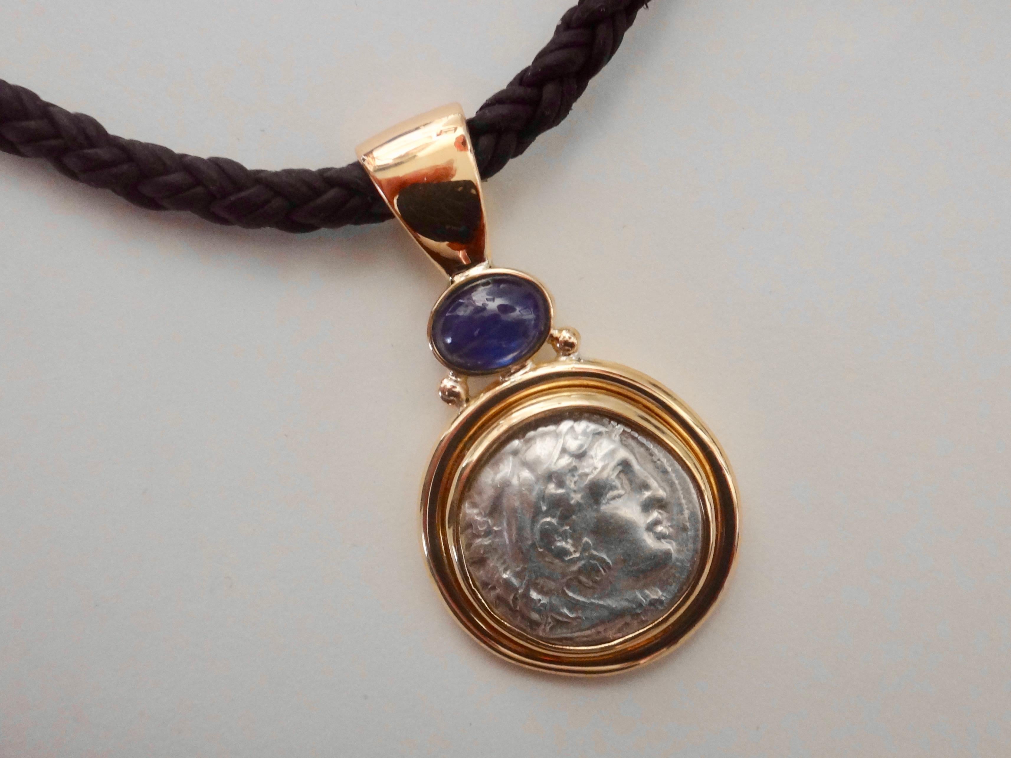 An authentic silver Alexander the Great III coin (Drachm coin 336 B.C.-very fine condition) is set in an hand fabricated 18k yellow gold pendant.  The setting is embellished with a bezel set cabochon sapphire of rich, blue color.  The extra large