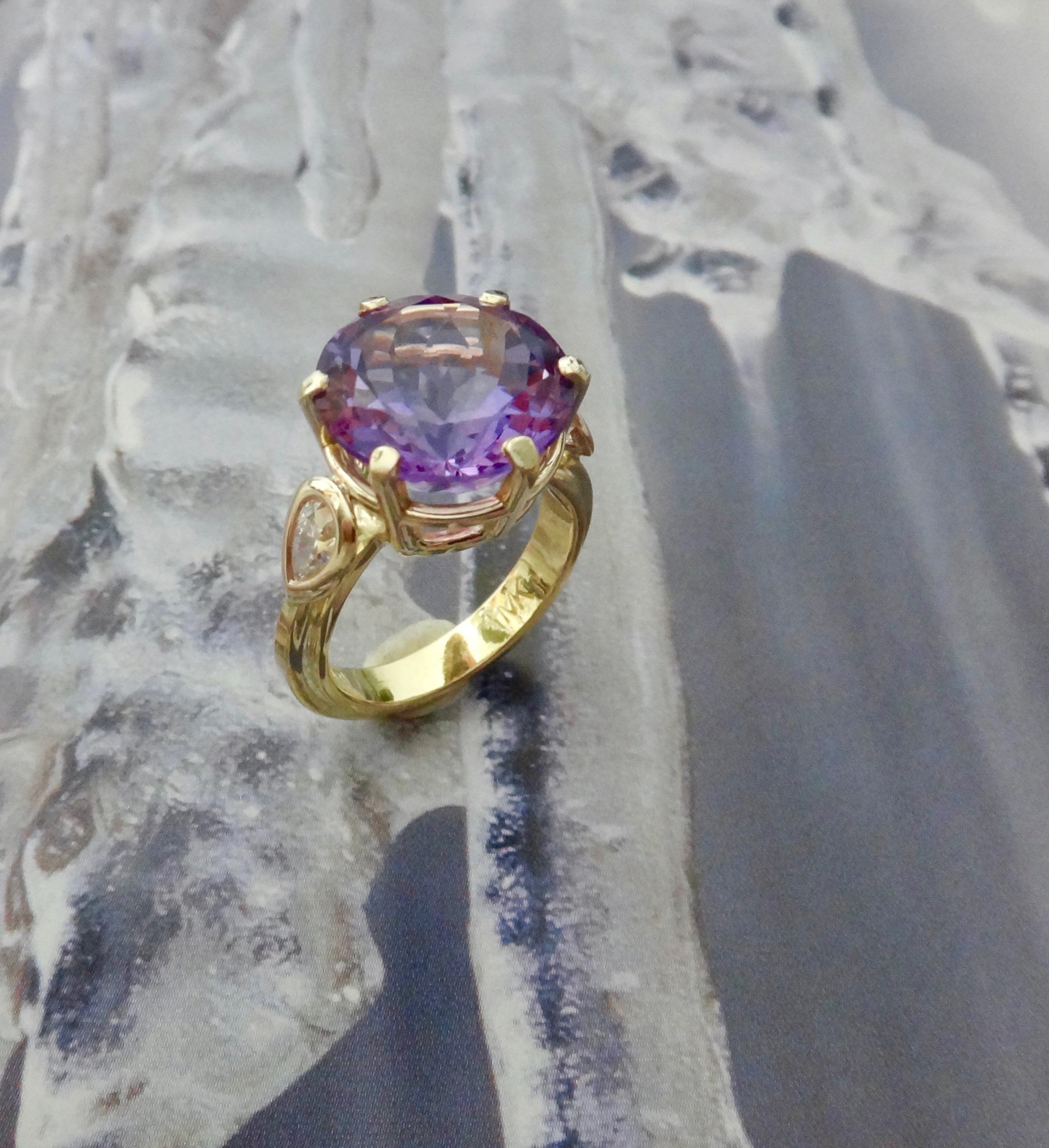 A round Portuguese cut amethyst is the centerpiece of this elegant cocktail ring.  The multitude of diamond shaped facets creates a very lively and flashy gem.  Flanking the center stone are two bezel set pair shaped diamonds.  The handmade 18k