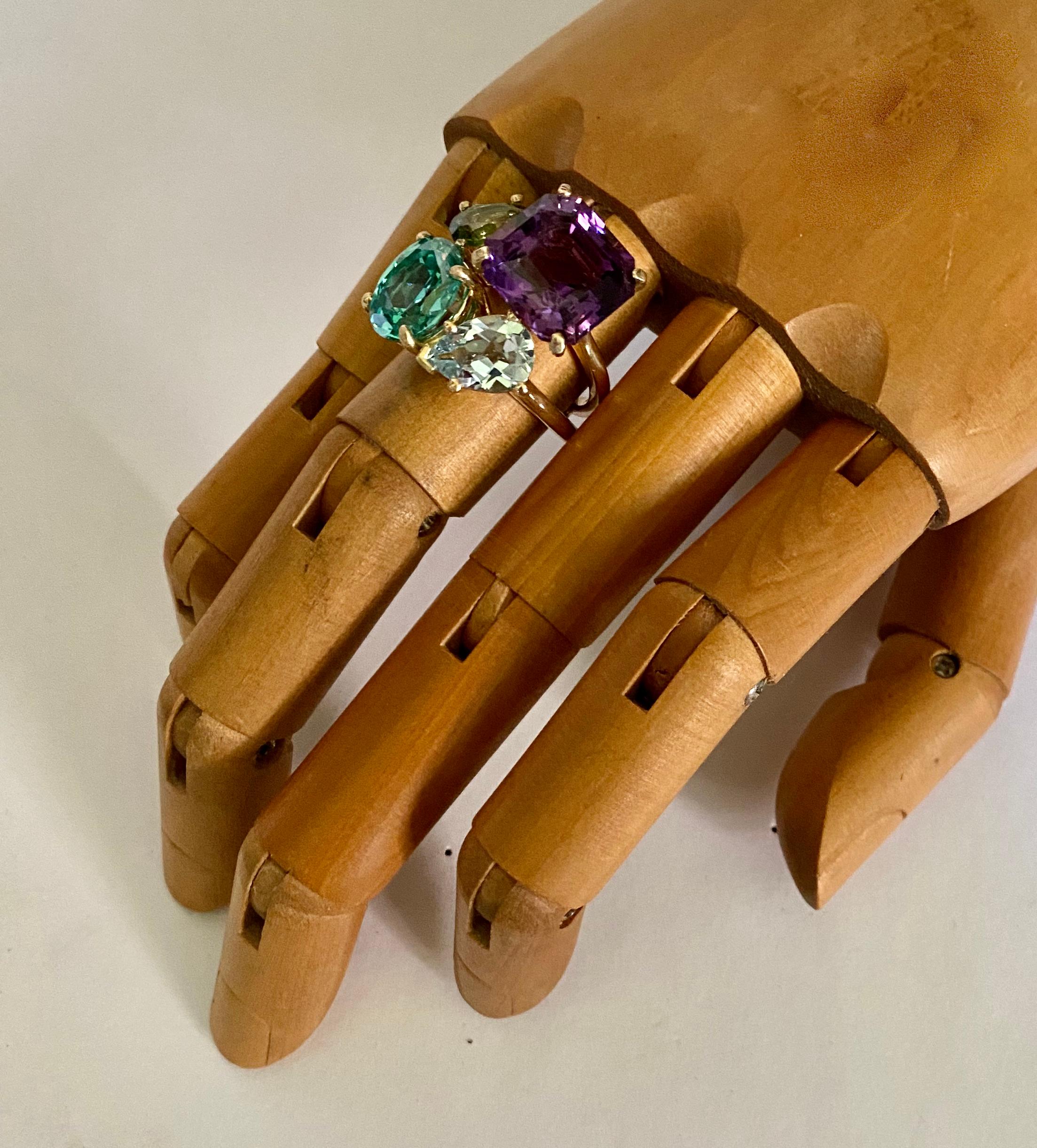 An amalgamation of colored gemstones come together to form this bold cluster cocktail ring.  A square cut amethyst (origin: Mexico)  is complimented by a pear shaped peridot (origin: Arizona), a glowing oval cut zircon (origin: Sri Lanka) and a