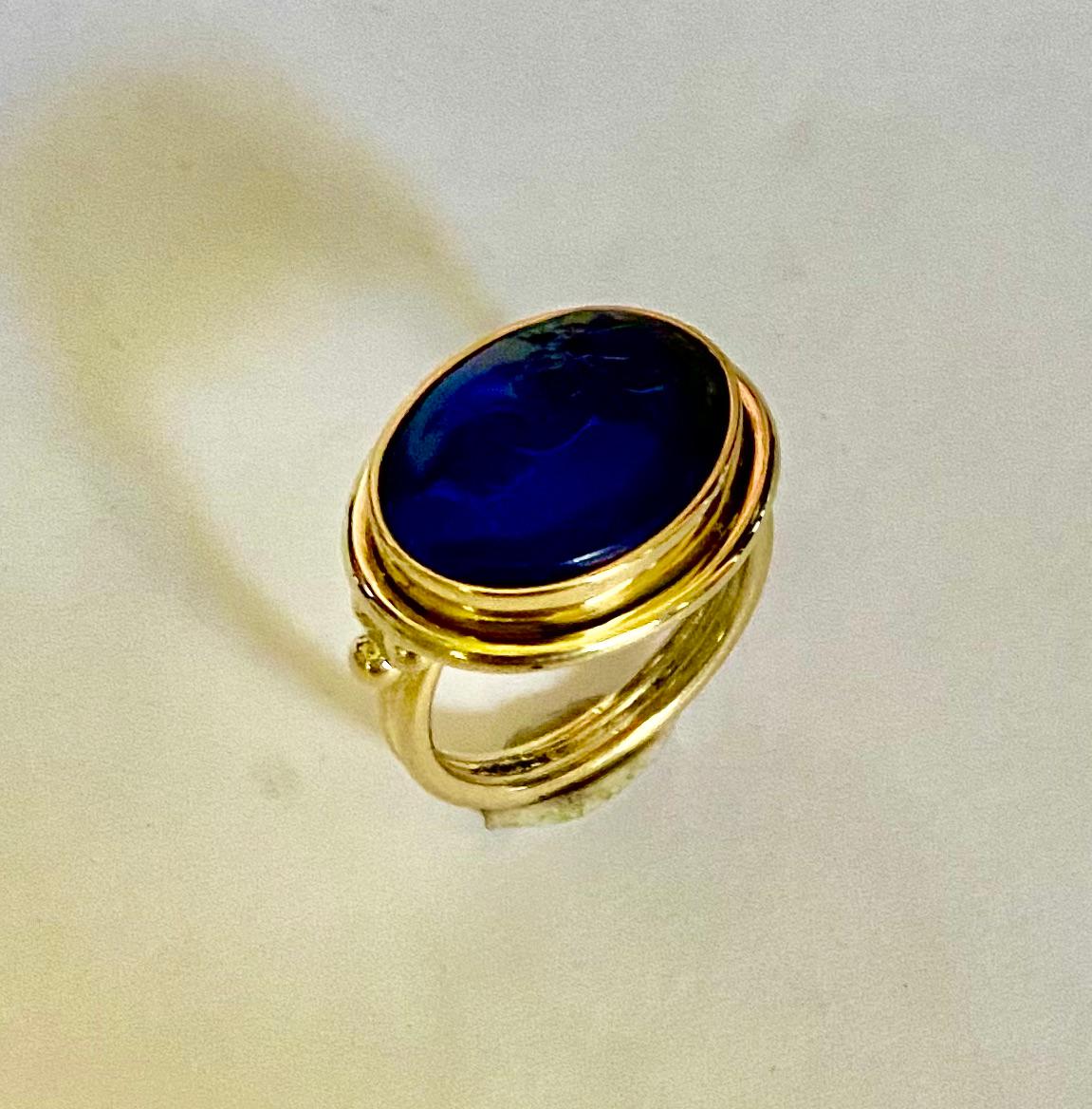 An antique Venetian glass intaglio is featured in this archaic style ring.  The exceptionally well carved cobalt blue intaglio features a charioteer.  The intaglio is set in an 18k yellow gold archaic style ring.  The inspiration for this piece