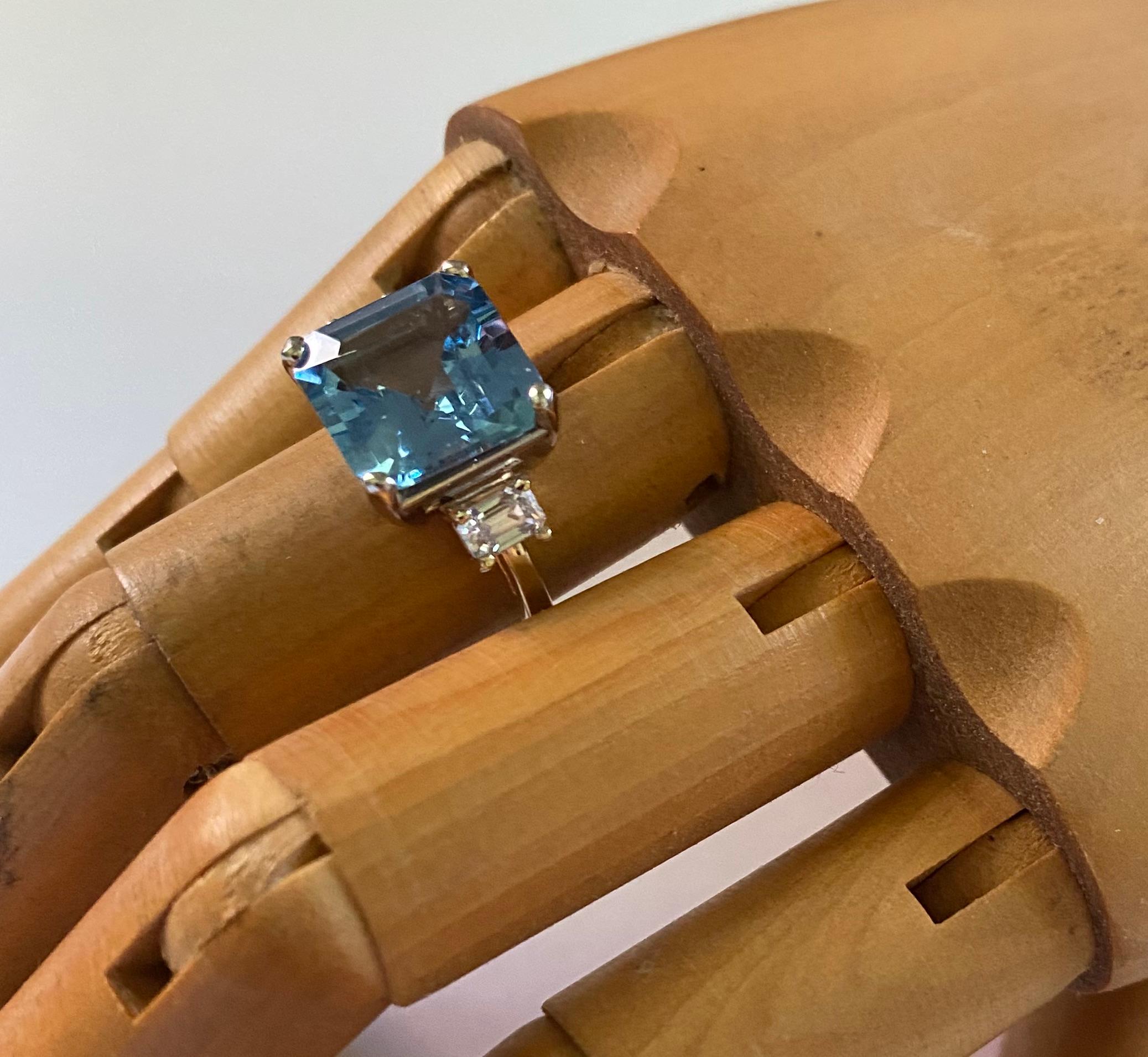 Aquamarine creates the centerpiece of this elegant three stone ring.  The aquamarine (origin: Brazil) is a classic blue color with no green undertones.  The gem has been fashioned into a square/ step cut.  It is well cut and polished.  It is flanked