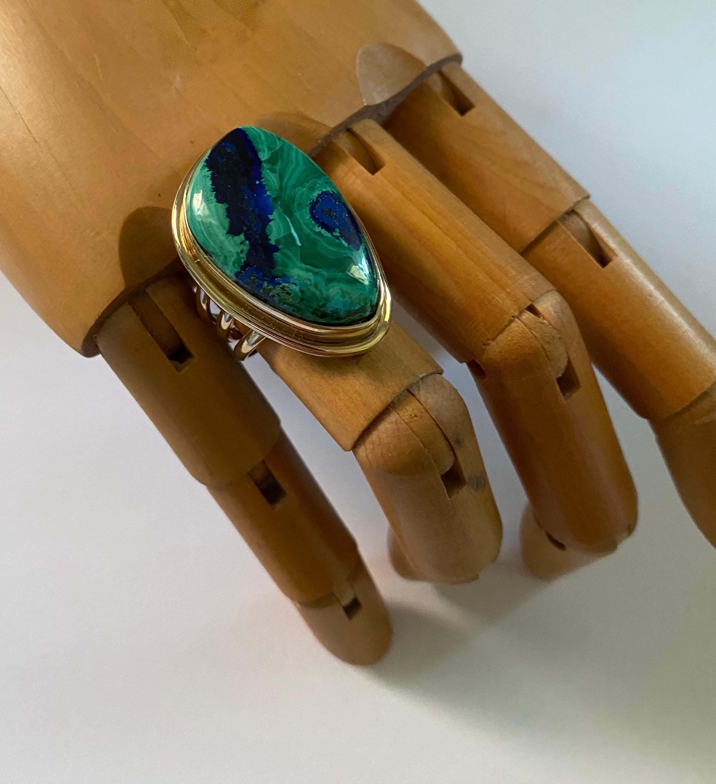 Azurite in malachite is showcased in this archaic style ring.  Sometimes called azurmalachite, this gem comes from Australia.  It is cut in a free-form shape and is polished to a glass-like shine.  The hand fabricated 18k yellow gold ring is