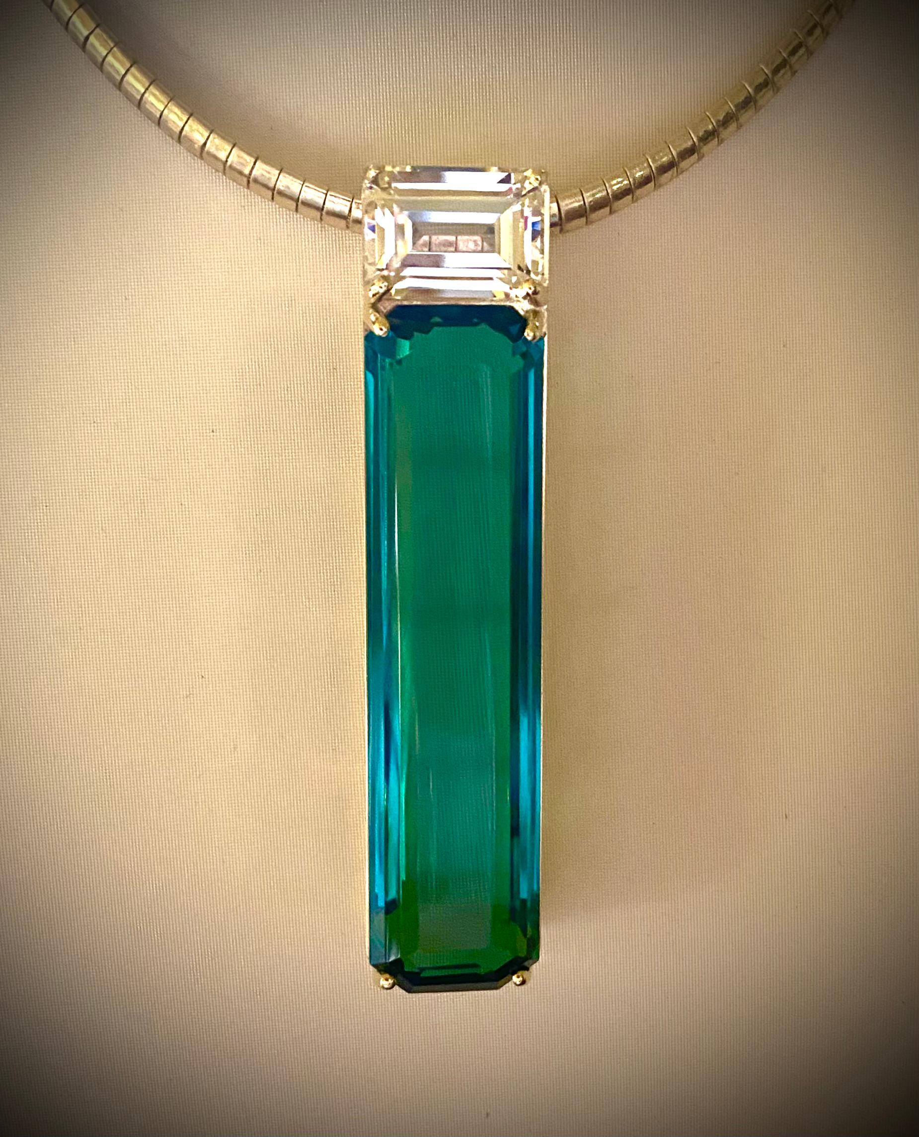 Topaz and sapphire are paired in this dramatic plinth pendant.  The highly unusual blue/green topaz (origin: Brazil) weighs 83 carats.  It has been expertly cut and polished into an elongated step cut.  The gem is exceptionally brilliant.  The topaz