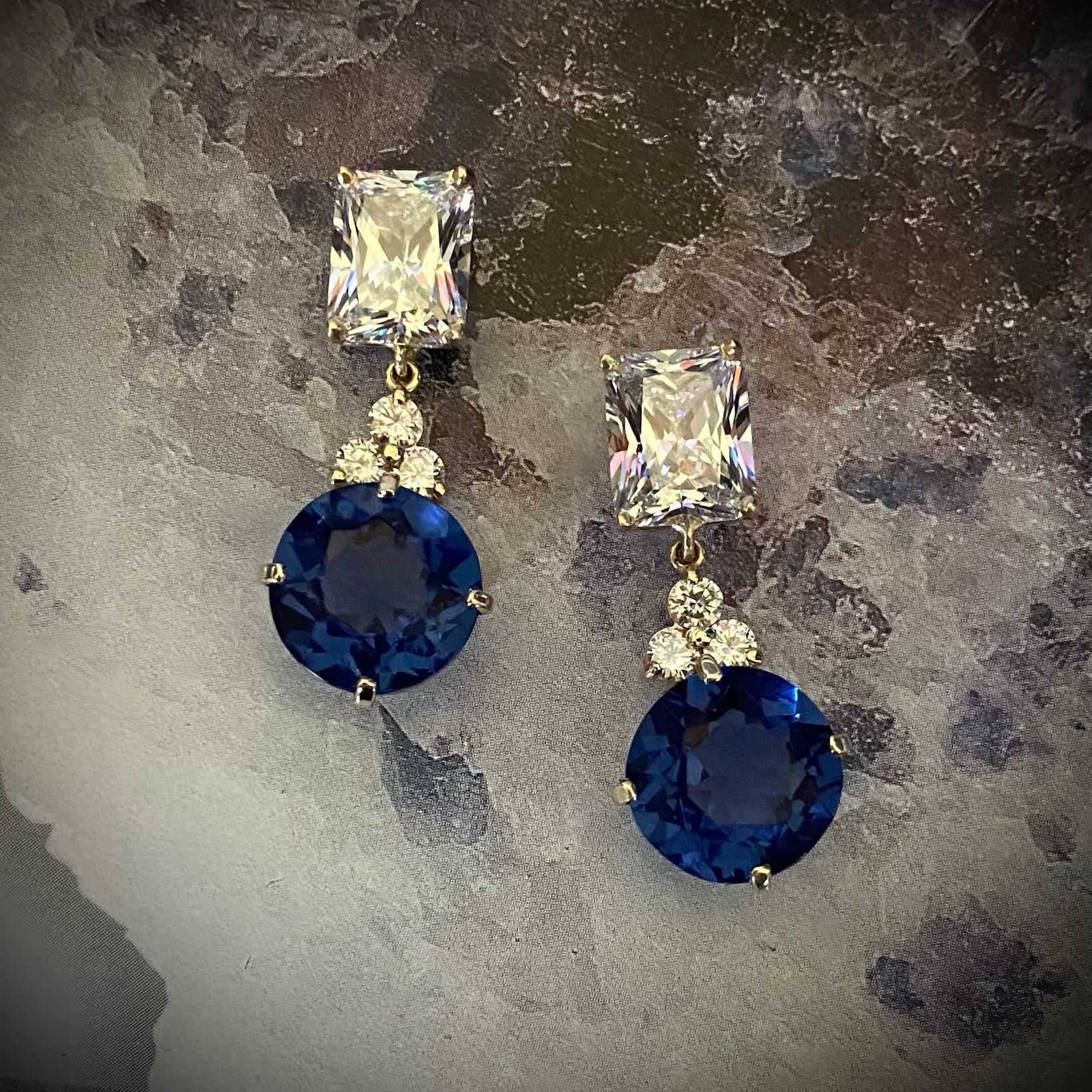 London blue topaz is featured in these stately dangle earrings.  The beautifully matched topaz (origin: Thailand) are a velvety, deep blue.  The round gems dangle from a cluster of three diamonds and topped with a radiant cut white sapphires