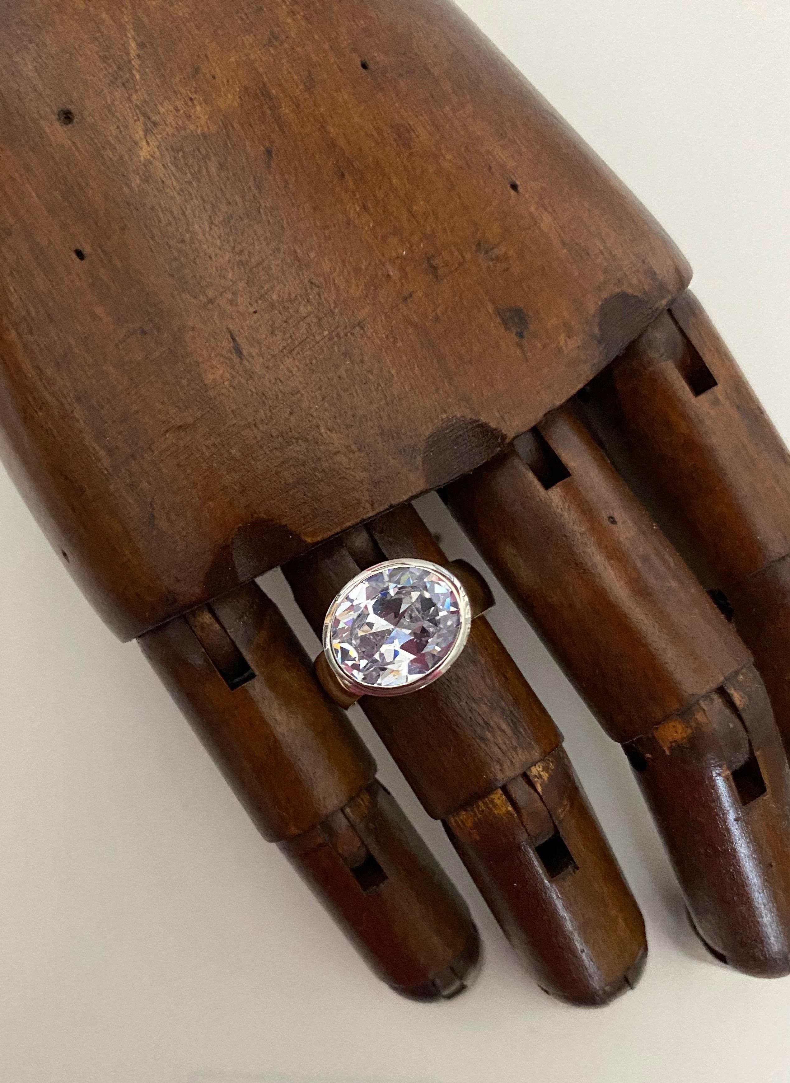 An oval cut silver sapphire of 5.63 carats is bezel set in this two-tone, 18k gold Leah ring.  This variation of the Leah features the gem set across the finger.  Expertly finished, the sapphire is well cut, polished and is completely colorless. 