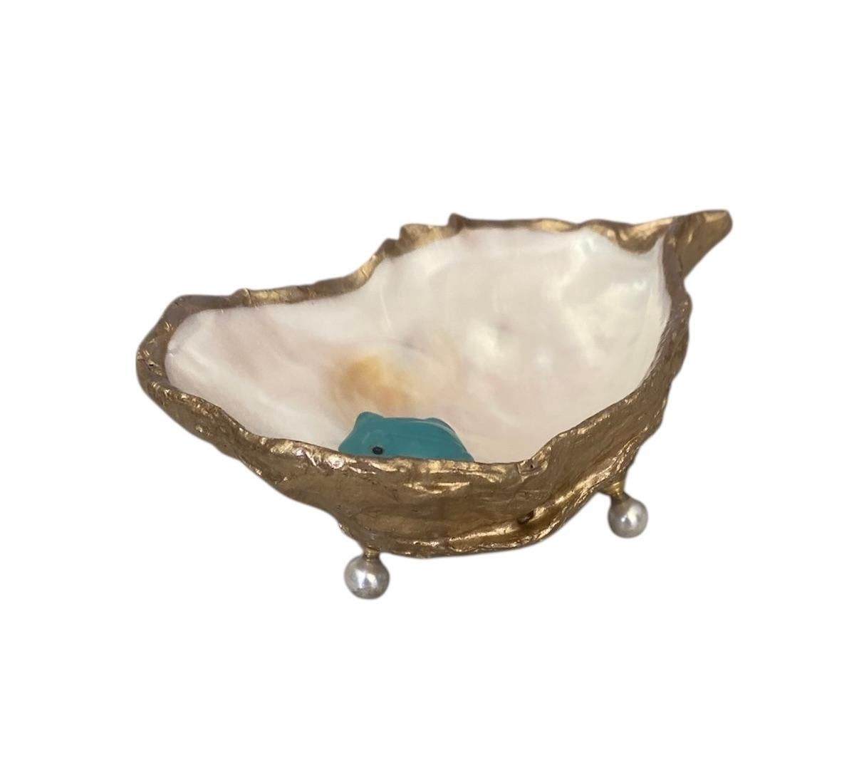 Une coquille d'huître lumineuse forme la base de ce charmant plat à anneaux.  L'intérieur de la nacre possède un éclat presque métallique.  Une grenouille en calcédoine bleue sculptée est nichée à l'intérieur.  La partie extérieure de la coquille a