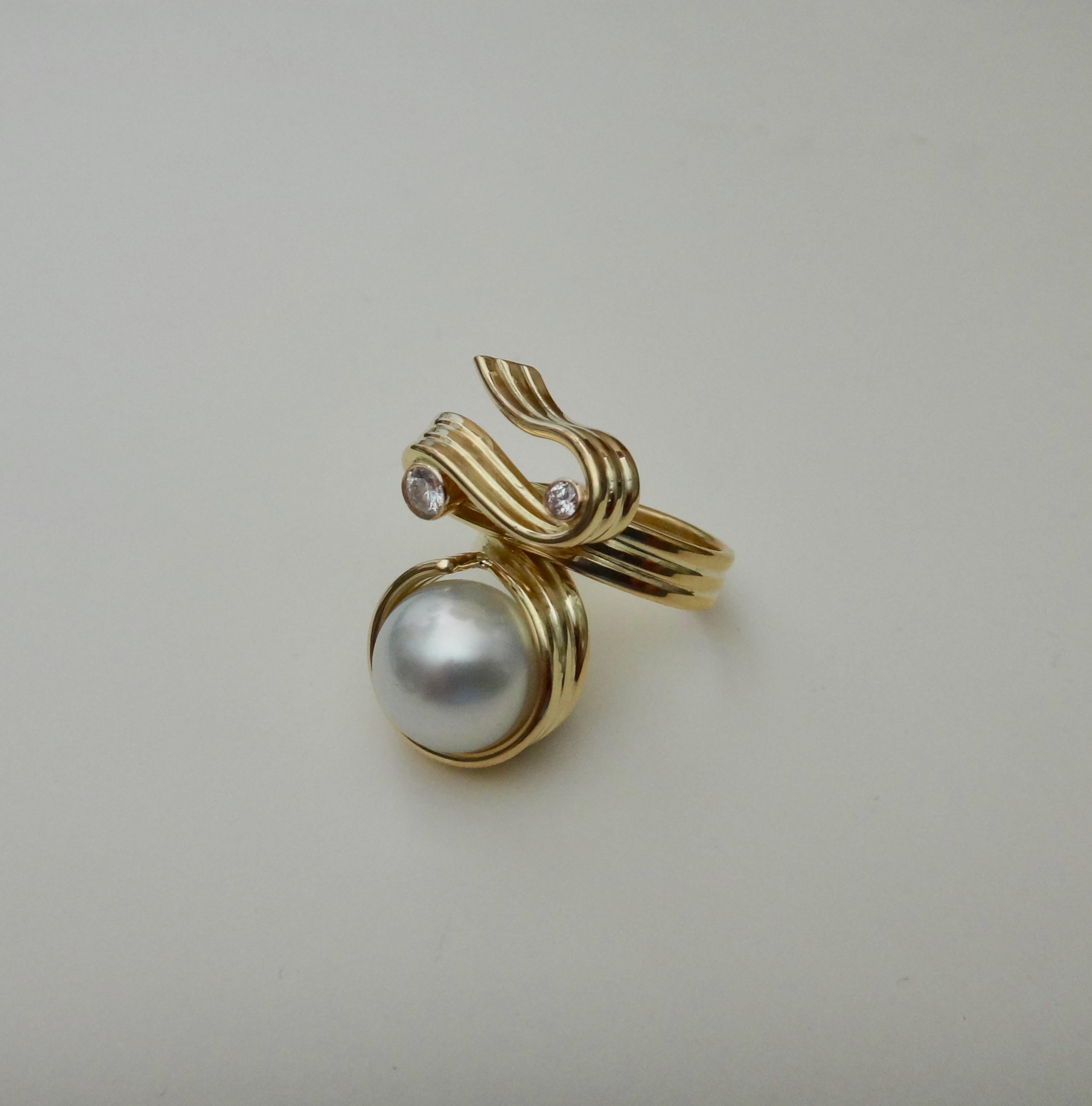 One continuous strip of 18k yellow gold wraps and twists around the finger in this Ribbon Candy ring.  Within the twists and turns is set a 12.5mm, White, gem quality  Paspaley South Seas pearl.  Further decorating the ring are two bezel set white