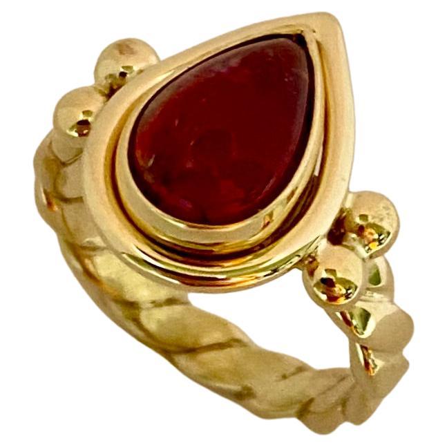 A pear shaped pink tourmaline is the focus of this archaic style ring.  The tourmaline (origin: Brazil) is intensely pink in color. It is well cut and polished to a glass-like finish.  The gem is set within and archaic style ring.  Similar examples