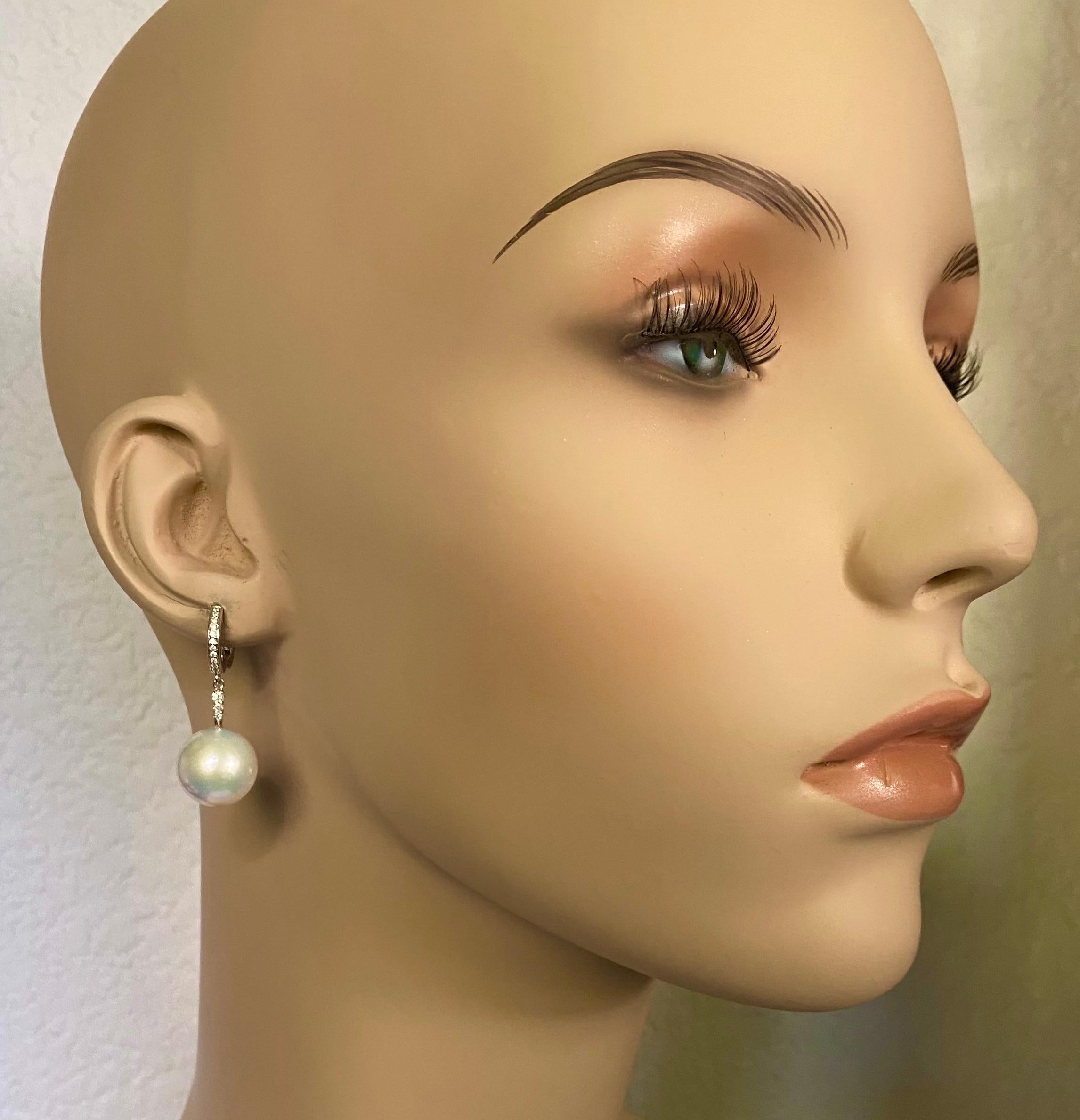 Diese eleganten und klassischen Ohrringe sind mit Südseeperlen besetzt.  Die runden, 13,5 mm großen Perlen sind reinweiß, gut abgestimmt und haben einen satten Glanz.  Sie hängen an Ohrringen aus Weißgold im Huggie
