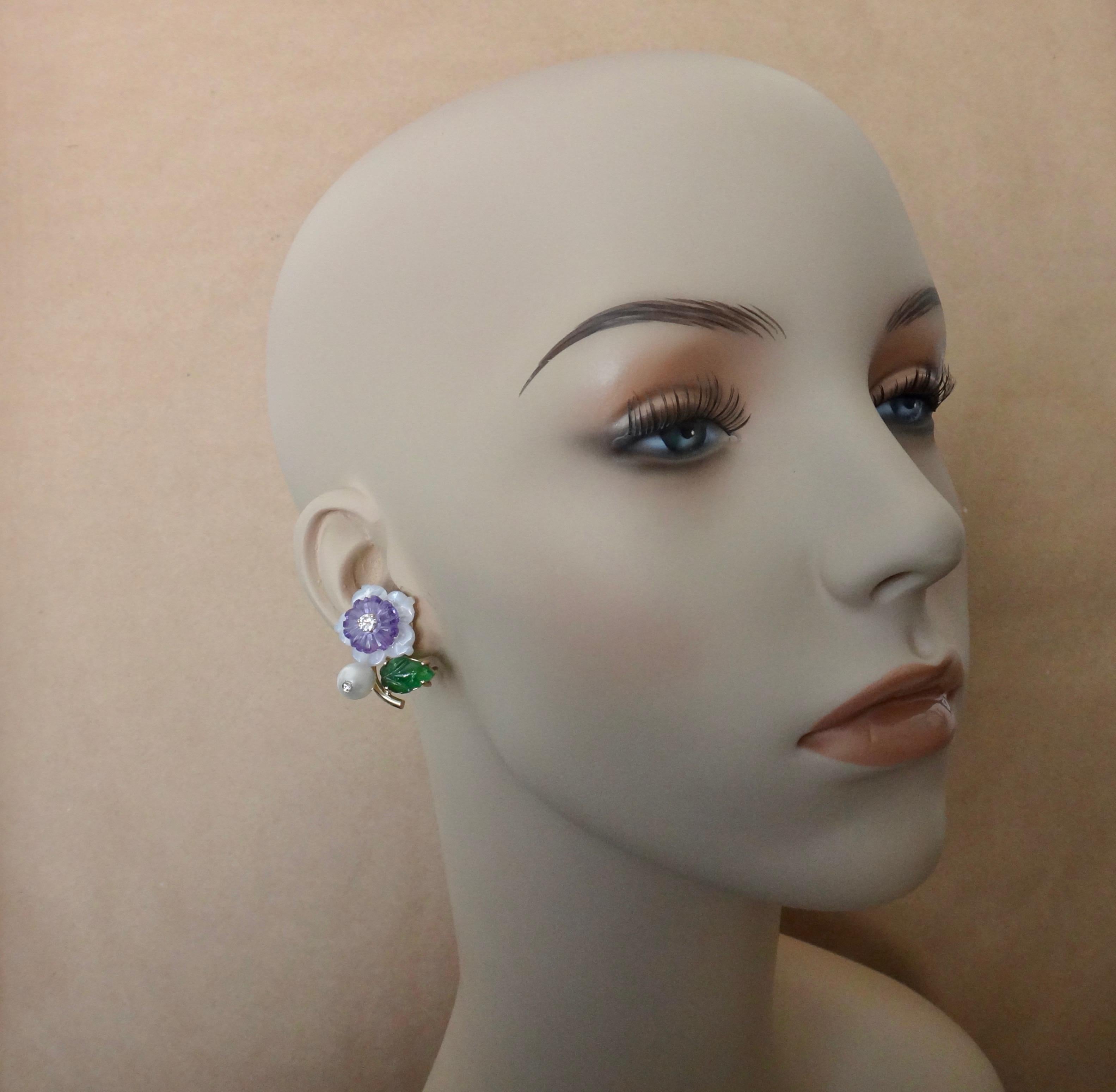 These whimsical flower earrings are reminiscent of compositions dating from the early 20th century.  The blooms are created from carved mother-of-pearl and amethyst along with white diamond centers.  The leaves are carved tsavorite (a green