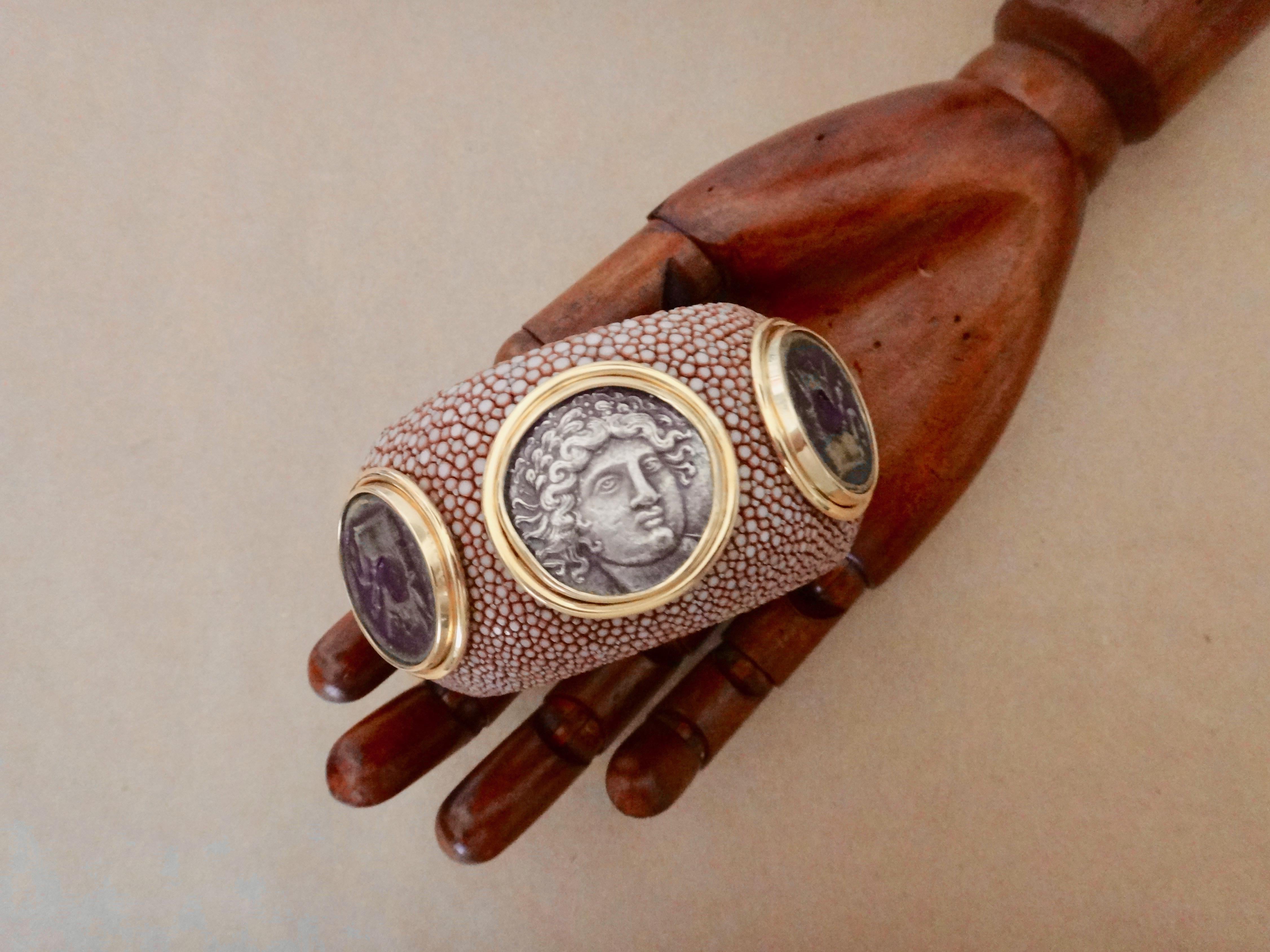 A milk chocolate colored shagreen (string-ray) cuff is decorated with three coins featuring images of Alexander the Great and the Minotour.  Cast in silver and bronze, the coins are set in handmade frames of 18k yellow gold and riveted onto the