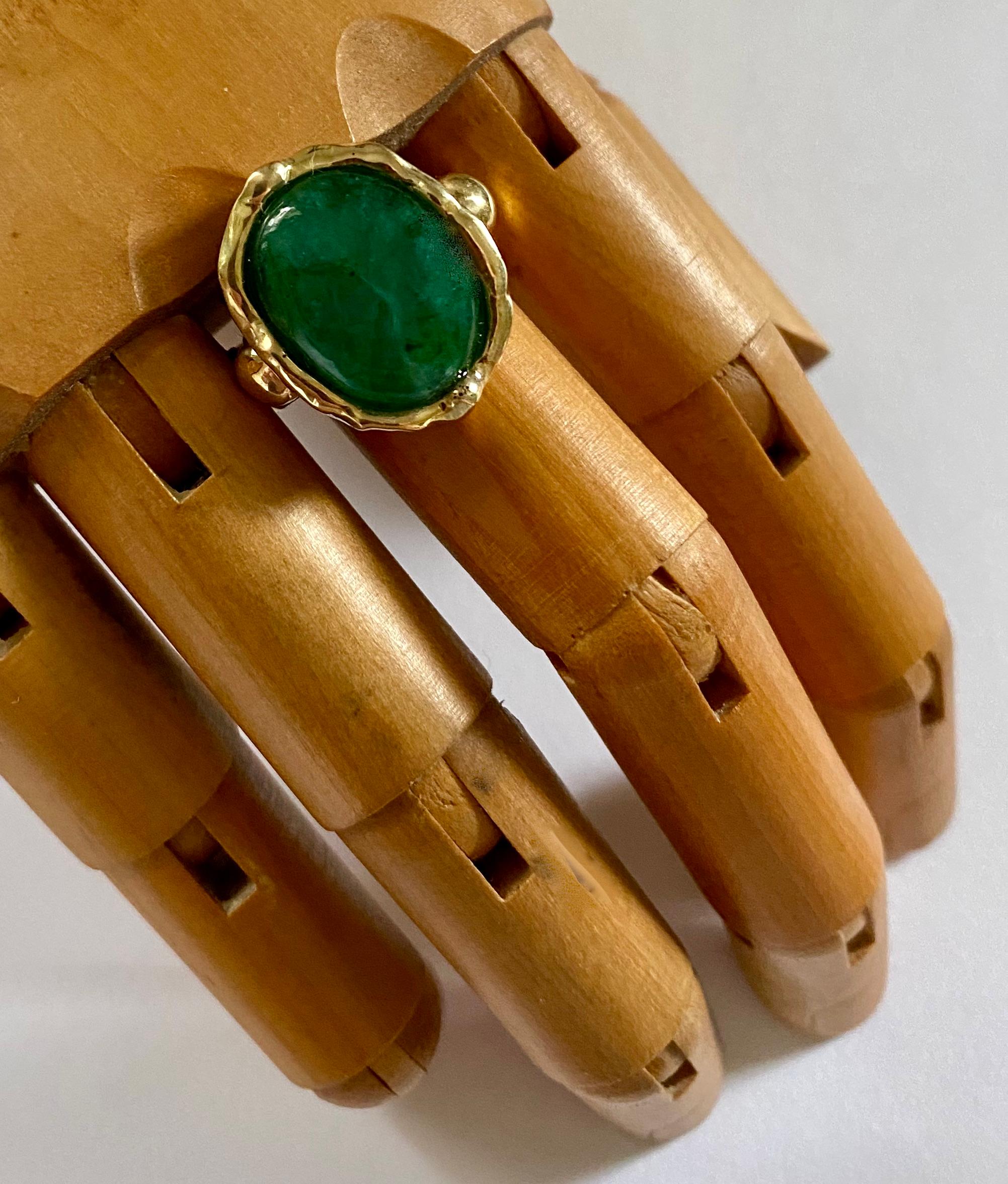 Zambian emerald is featured in this archaic style ring.  The emerald is cabochon cut.  It possesses a rich green color, is semi-transparent and is well cut and polished.  It is set in a ring sculpted in 18k yellow gold.  The style if the mounting