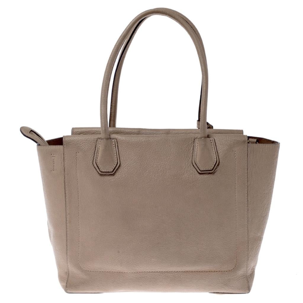 Featuring a chic and fabulous style, this Michael Kors tote is modern. Crafted from leather in stunning beige, the tote features dual handles and a padlock. It opens to a spacious leather interior that houses an open compartment. The tote comes with
