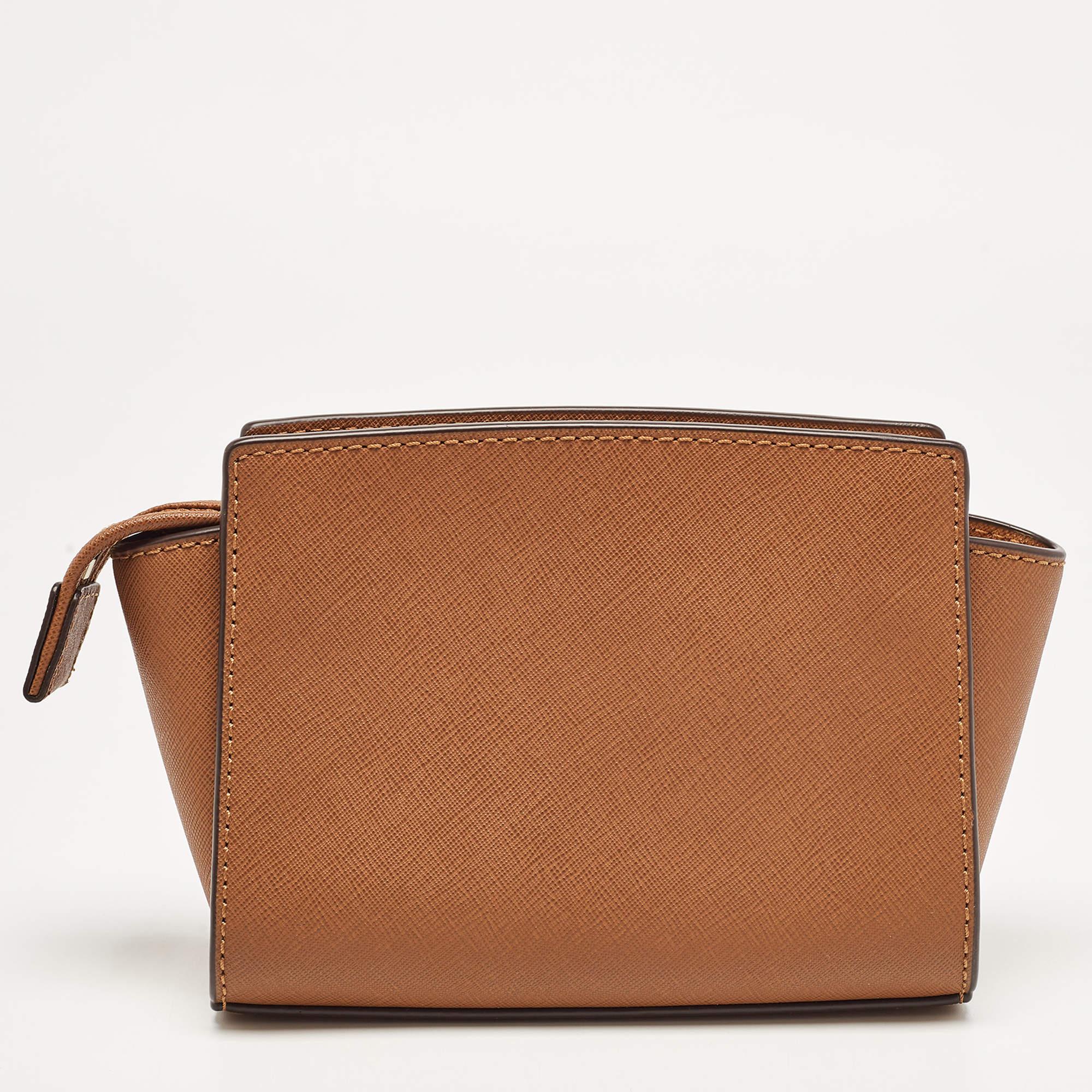 This mini Selma crossbody bag from Michael Kors is a stunning creation. It is designed using brown leather on the exterior and features a gold-toned logo accent on the front and a shoulder strap. It is equipped with a fabric-lined