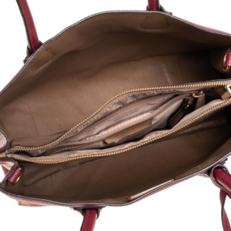 Featuring a chic and fabulous style, this Michael Kors tote is modern. Crafted from grained leather in a lovely burgundy shade, the tote features dual handles, brand logo detailing on the front, and a dangling padlock accent. It opens to a spacious