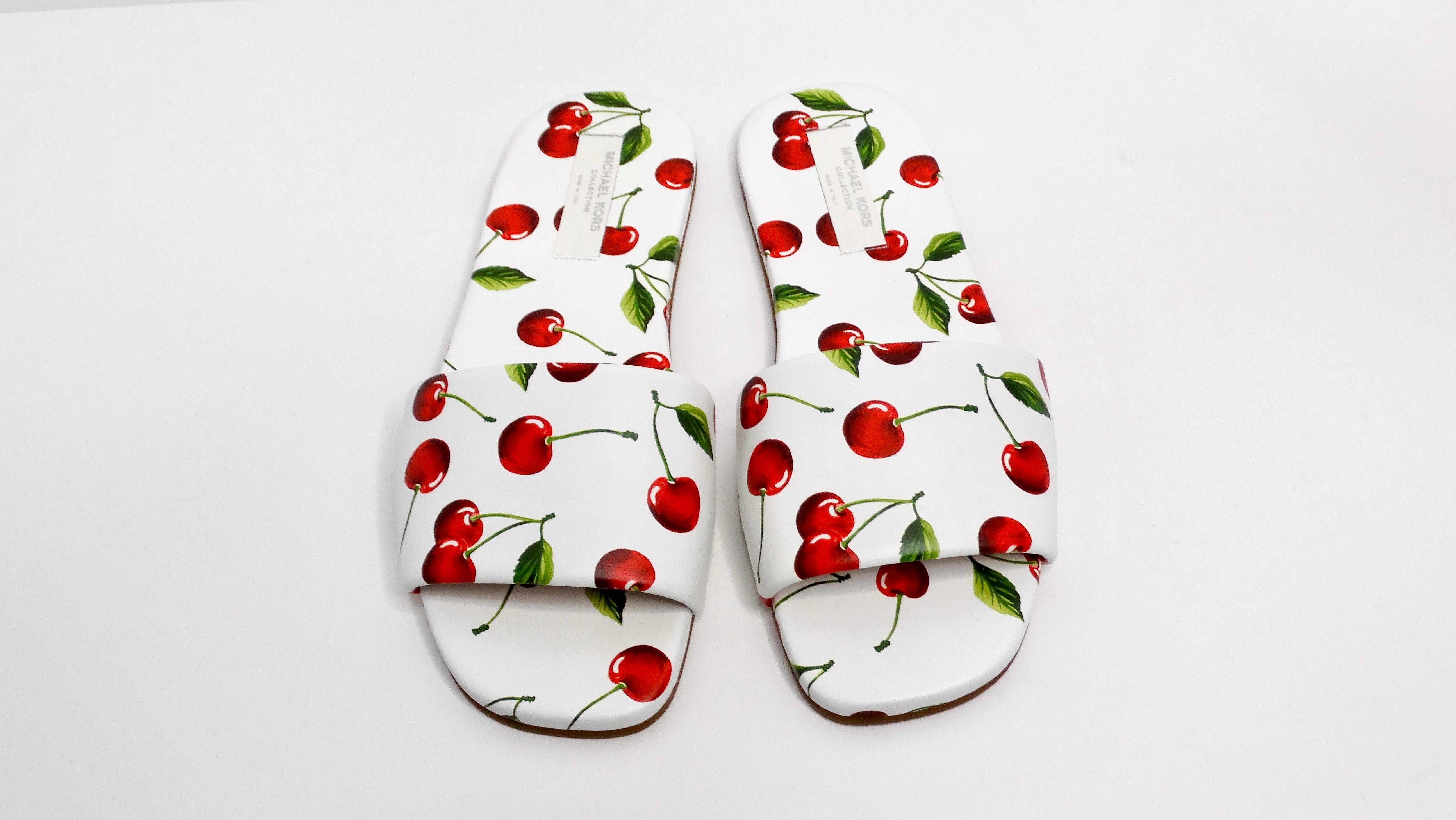 Step into fun with the Michael Kors Collection Cherry Print Leather Delphine Slides, a playful and chic footwear option that embodies effortless style. Featuring a white base adorned with vibrant red cherries and lush green stems, these slip-on