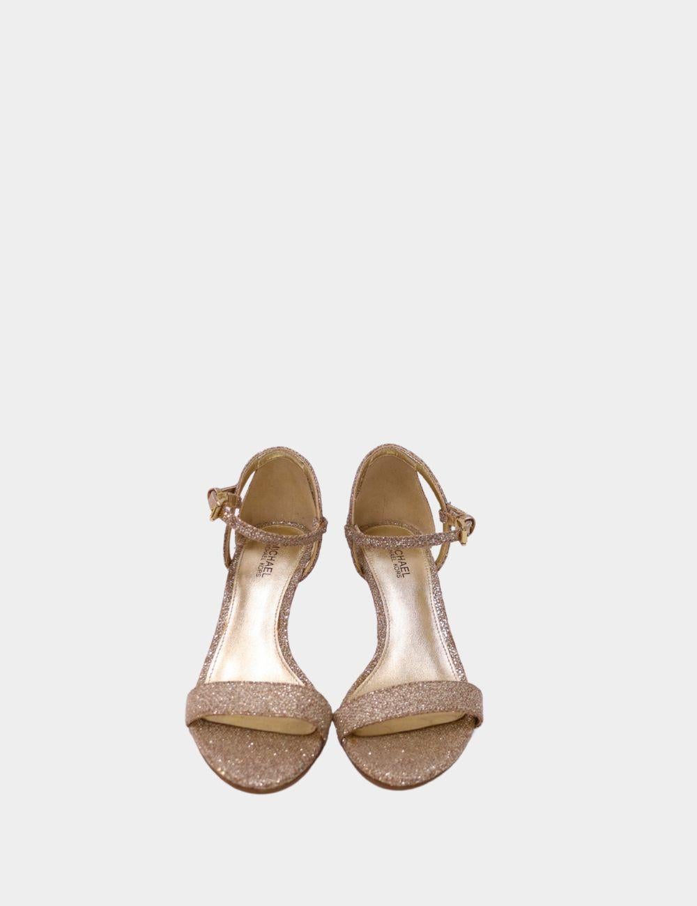 Step into timeless elegance with the Michael Kors Gold Shimmer Strappy Heel, a perfect blend of sophistication and sparkle. Crafted with a delicate ankle strap and secure buckle fastening, this mid-heel sandal offers both comfort and glamour. Its