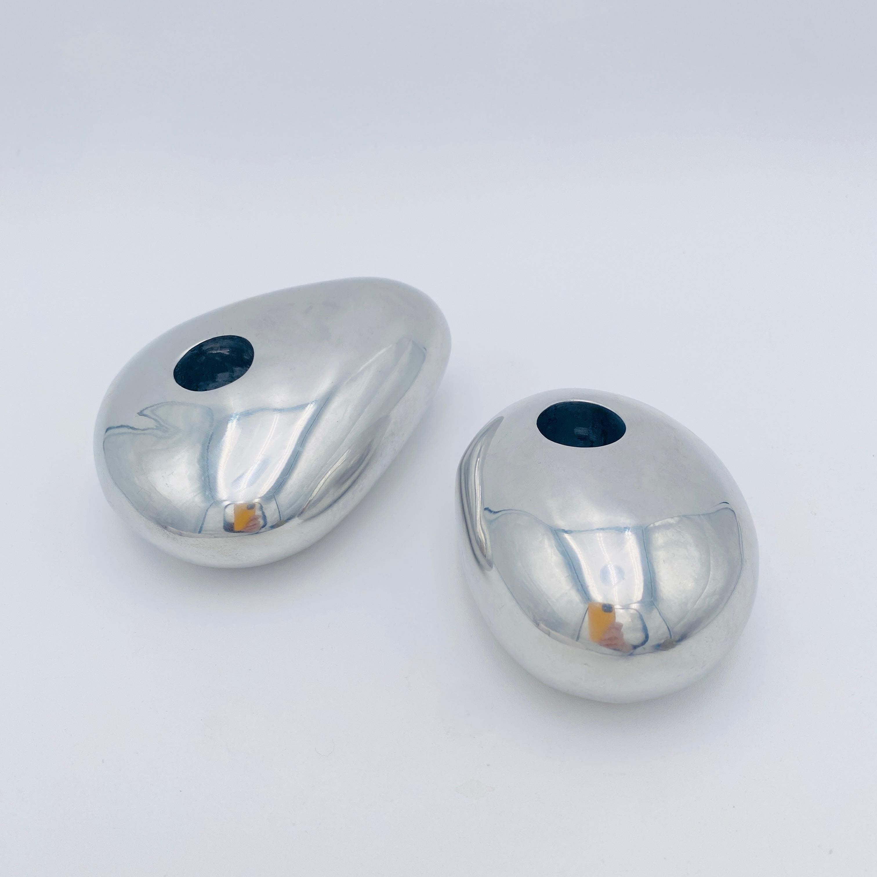 A pair of rock-shaped candlesticks designed by Michael Lax Design Grainware circa 1990. These post-modern candle holders are made of polished aluminum. The bottom of each candle holder has the maker's mark and model number. Together they weigh