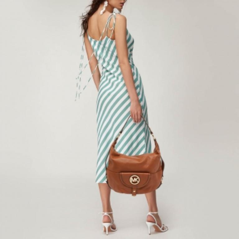 Este hobo Michael Kors Fulton seguro que llama mucho la atención. Se ha diseñado con piel marrón y se cierra con una cremallera. Este bolso está provisto de una sola asa y un bolsillo delantero con el logotipo MK. Tiene un interior forrado de nailon
