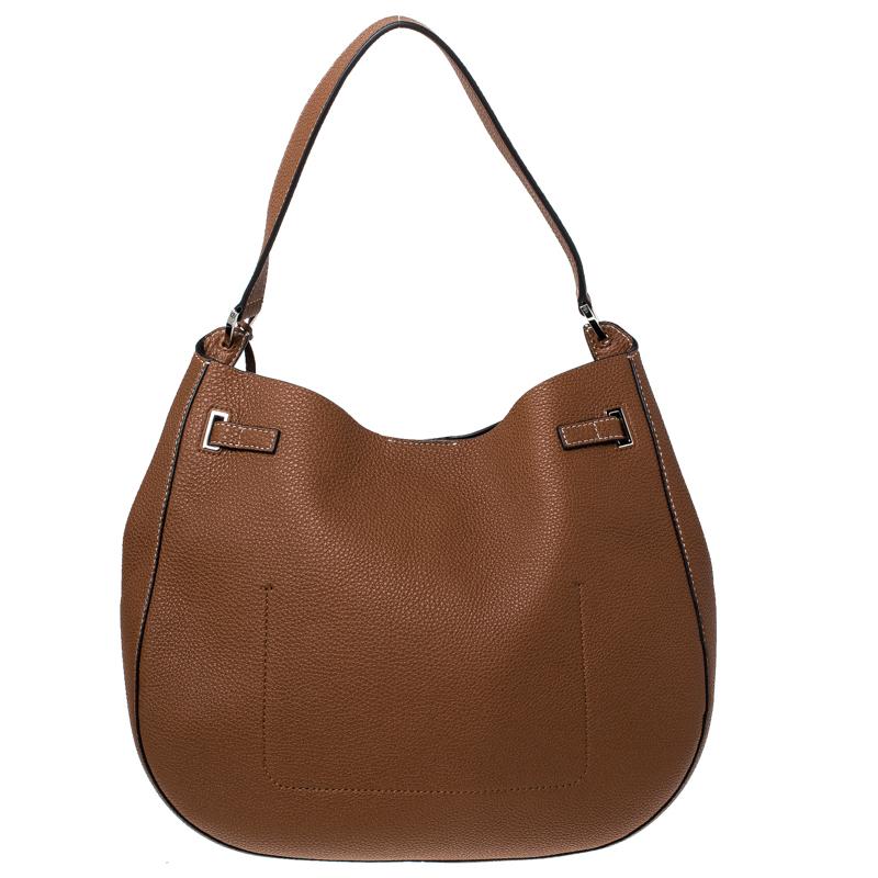 High on style, carry this handbag from Michael Kors without compromising on style. This dashing bag in tan colour is enhanced with silver-tone hardware and features a single handle. It has a suede lined interior that can store all your essentials