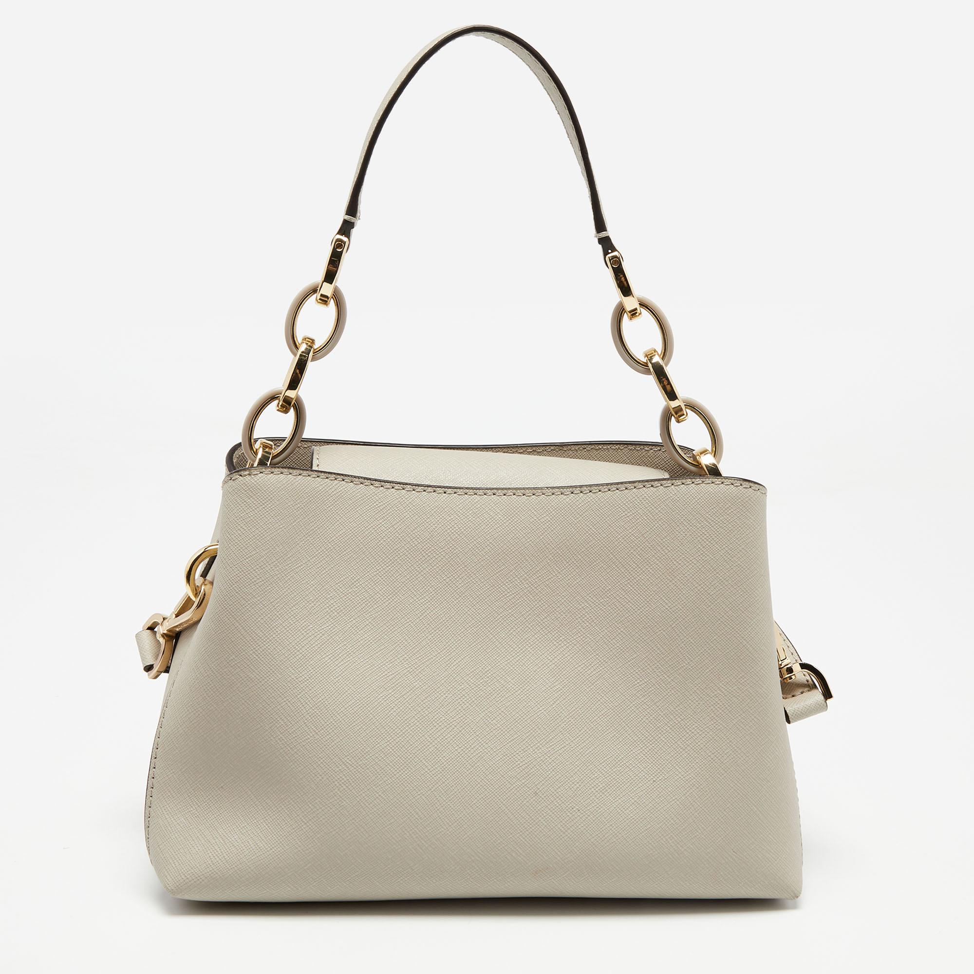 This MICHAEL Michael Kors bag proves minimalism can be classy. Made from leather, it exhibits a brand signature on the front, a shoulder strap, and a single handle. The fabric-lined interior of the bag is divided into two compartments by a zipper