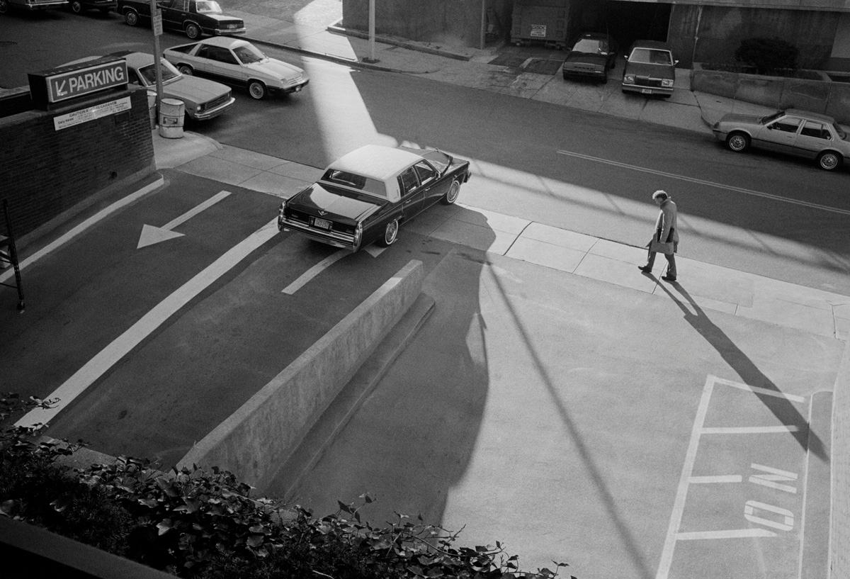 Michael Ormerod Black and White Photograph - Man Walking Past Parking Lot - Classic car, Cadillac, Street photography
