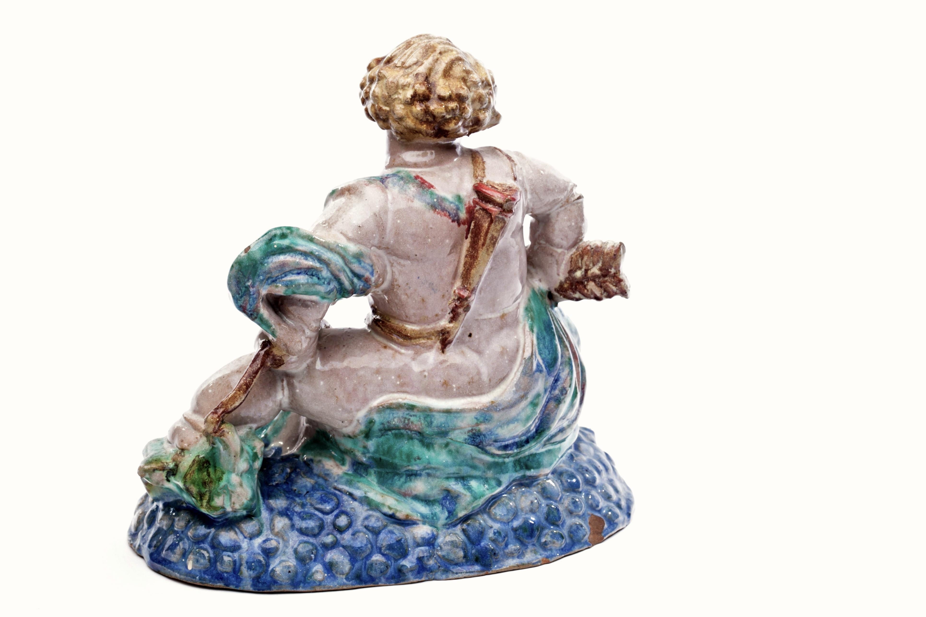 Exceptionnel Putto autrichien dans le style de Michael Powolny avec arc, flèche et carquois sur le dos, assis sur un lit coloré de bulles bleues. Magnifique sculpture en grès aux émaux riches et subtils. Des pieds fabuleux et trapus.