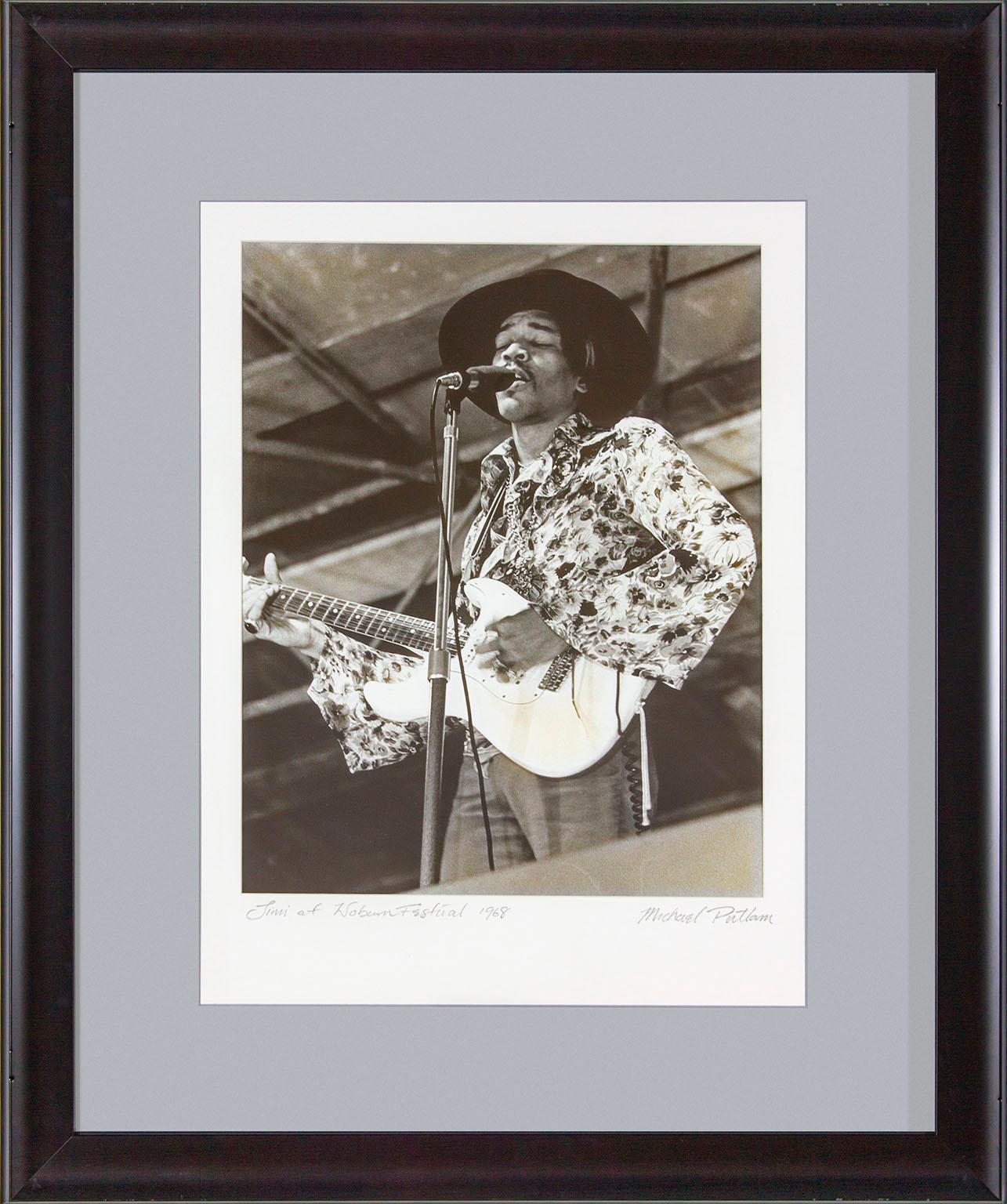 "Jimi at Woburn Festival 1968" framed black and white photograph by Michael Putland of Jimi Hendrix at the July 6, 1968, Woburn Music Festival in England.  "Jimi at Woburn Festival 1968" hand written on front lower left corner. "Michael Putland"