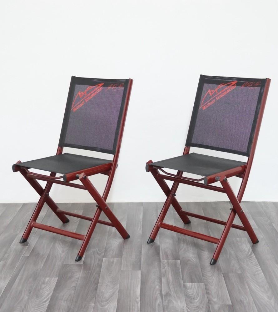 Iconic set of two red lacquered metal folding chairs with black technical fabric seat and back, both personalized with Michael Schumacher's logo and signature.

Produced as official merchandise in the early 2000s, they represent a rare collector's