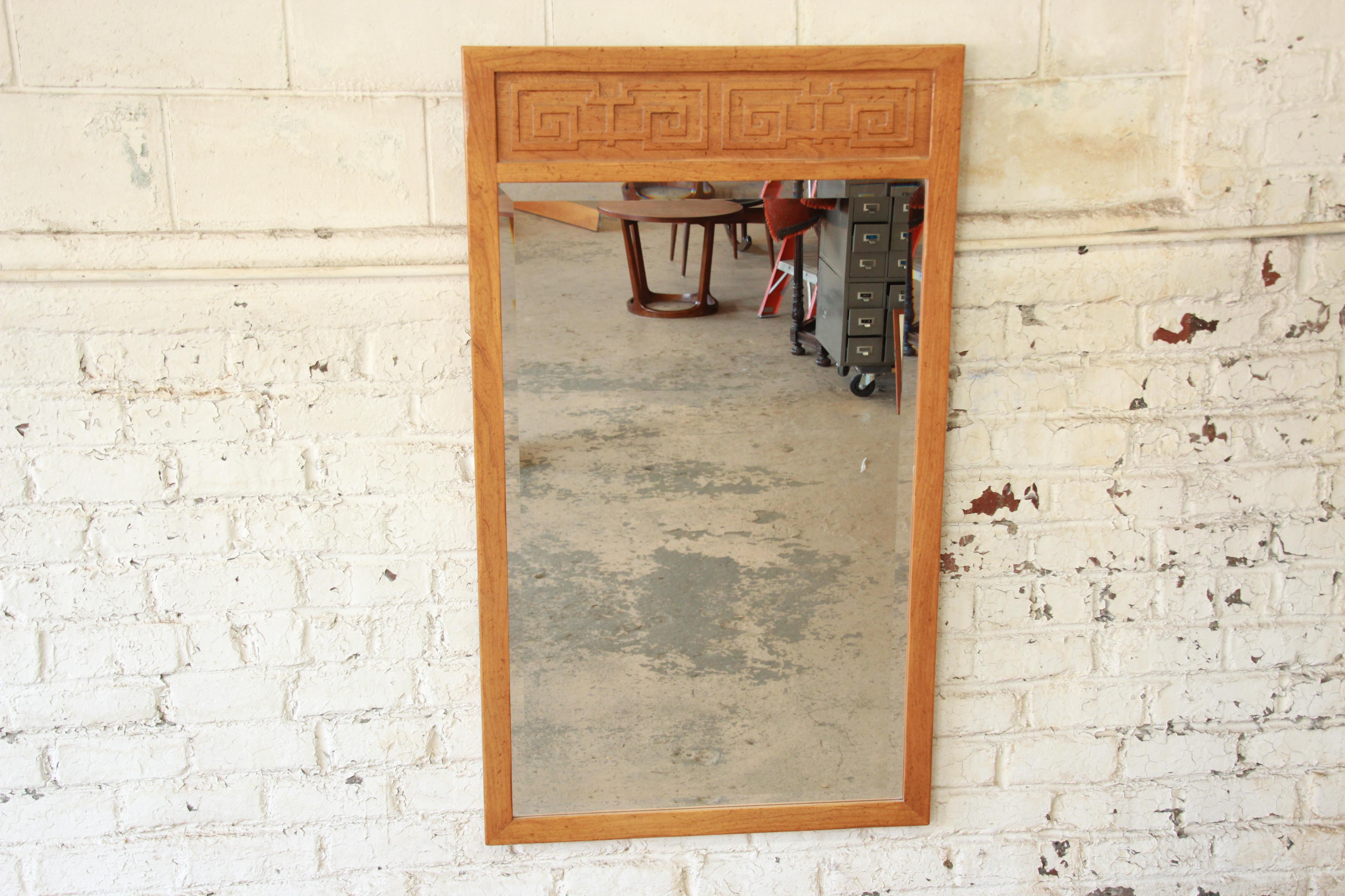 A stunning Hollywood Regency chinoiserie beveled wall mirror from the Far East collection by Michael Taylor for Baker Furniture. The mirror features a gorgeous solid elm wood frame with carved Asian details. The original Baker label is present on
