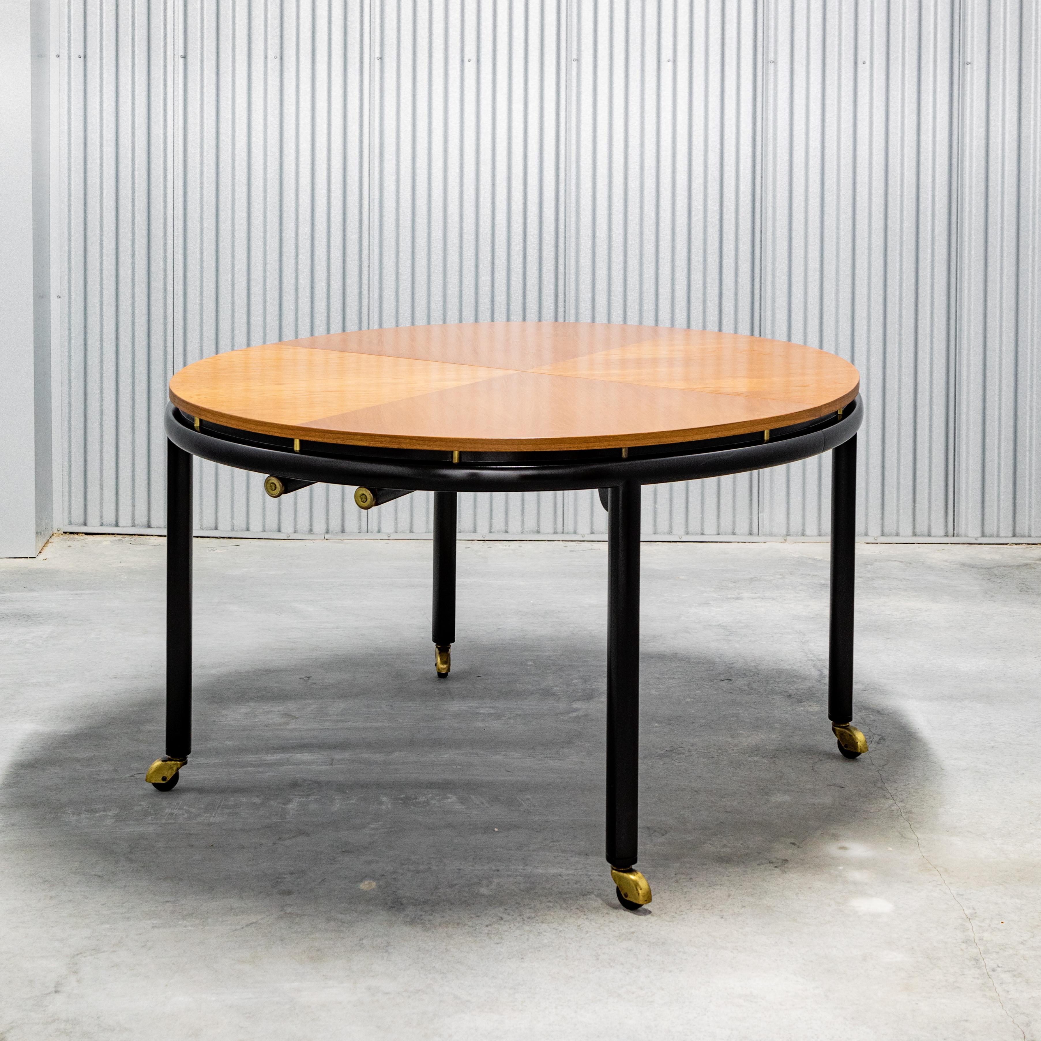 Elliptical dining table by Michael Taylor for Baker, book matched wood grain top, with black lacquered base and antique brass stand-offs at apron, on castors, includes three leaves and the original table pads, U.S. circa 1970's.