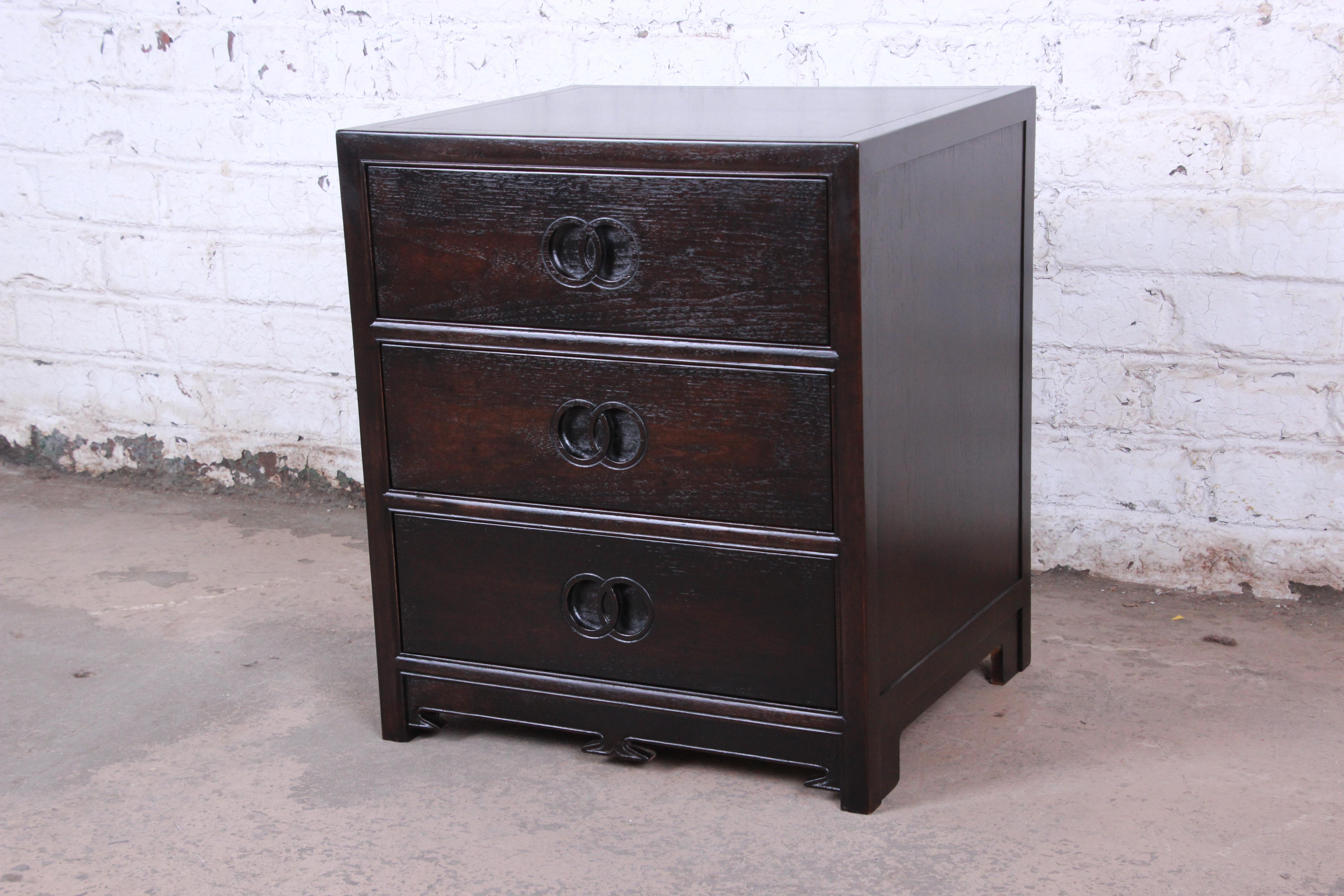 A beautiful, newly refinished Hollywood Regency chinoiserie three-drawer bachelor chest or nightstand designed by Michael Taylor for his Far East Collection for Baker Furniture. The chest features gorgeous wood grain, Taylor's iconic carved