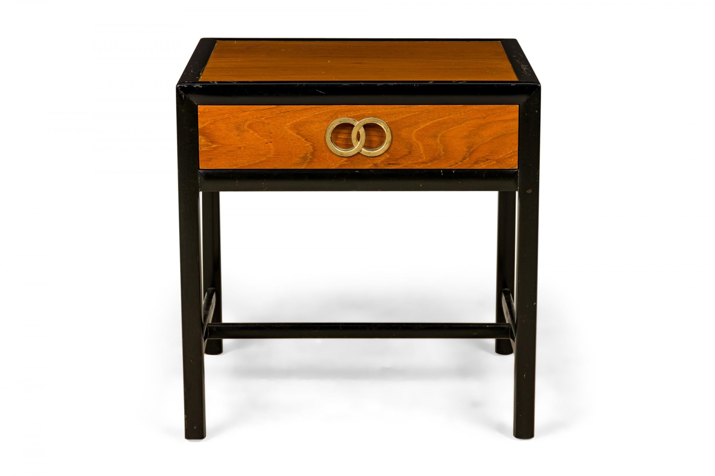 American Mid-Century rectangular nightstand / bedside table with a wooden top and drawer front with and interlocking ring design polished brass drawer pull in a black painted and lacquered frame with a stretcher base. (Michael Taylor for Baker