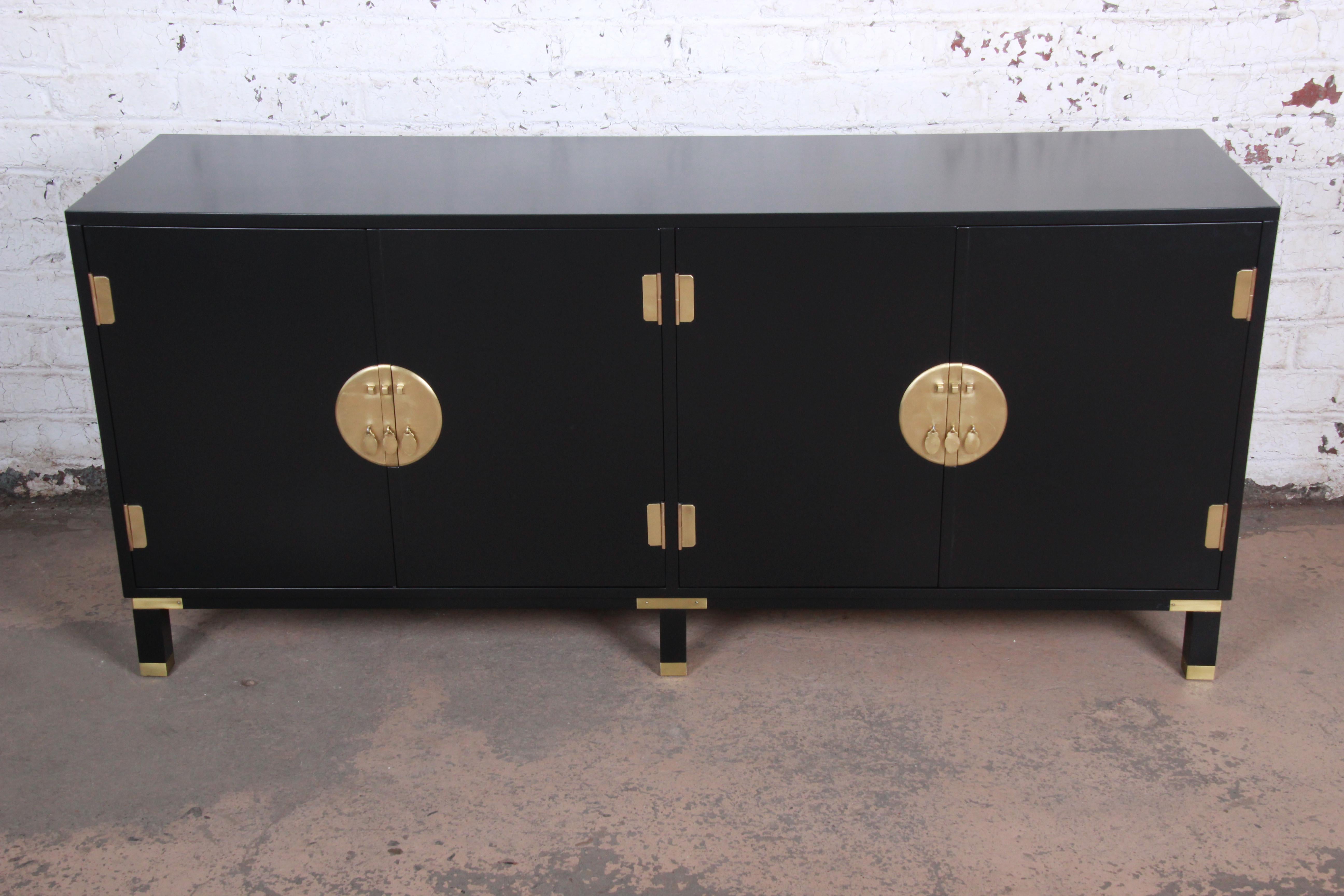 An exceptional Hollywood Regency chinoiserie sideboard credenza by Michael Taylor for Baker Furniture. The credenza features stunning ebonized wood with brass feet and accents and original Asian-inspired brass hardware. It offers ample storage, with