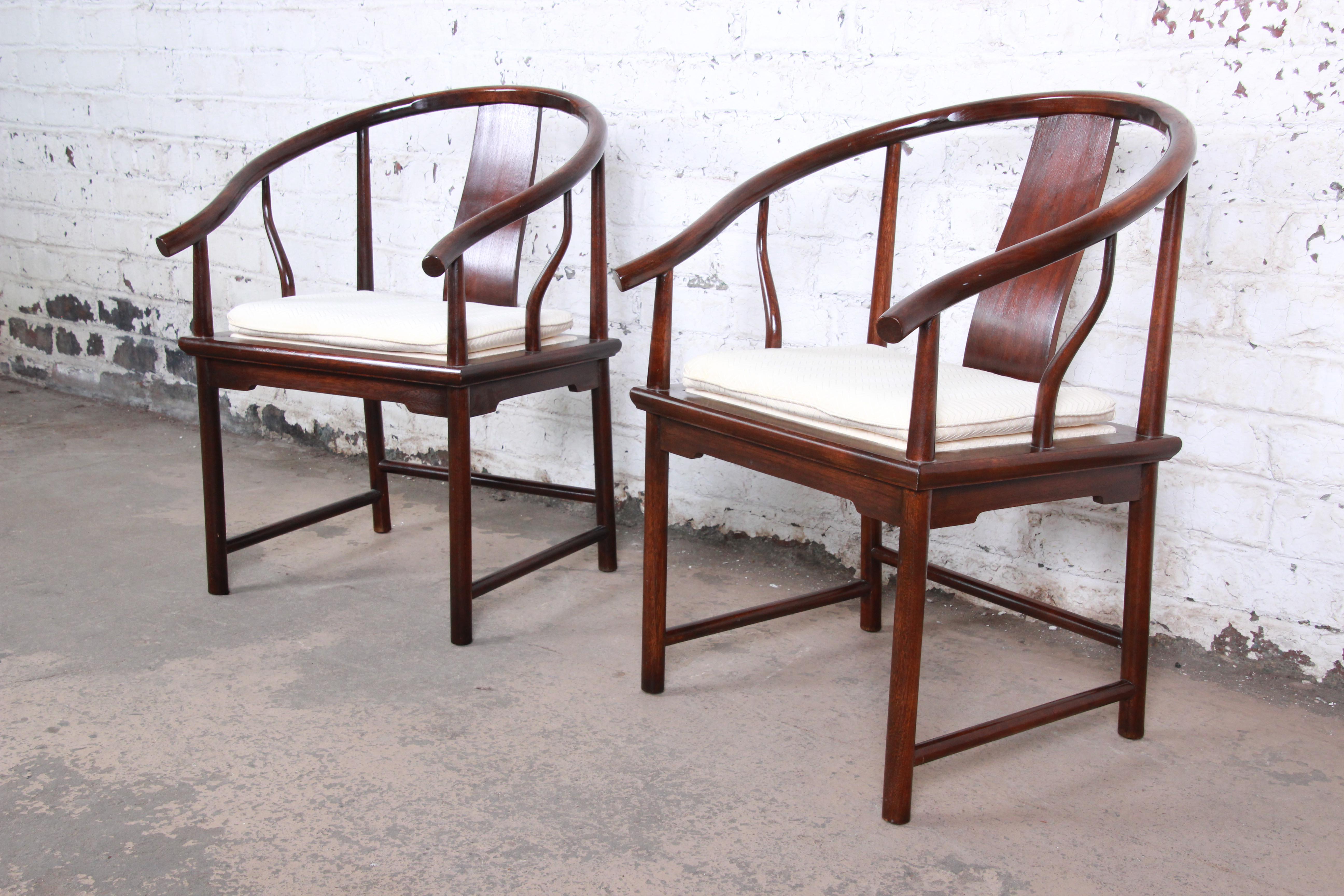 An exceptional pair of Hollywood Regency chinoiserie club chairs designed by Michael Taylor for his Far East collection for Baker Furniture. The chairs feature solid walnut frames with an Asian-inspired horseshoe design. The ivory upholstery with