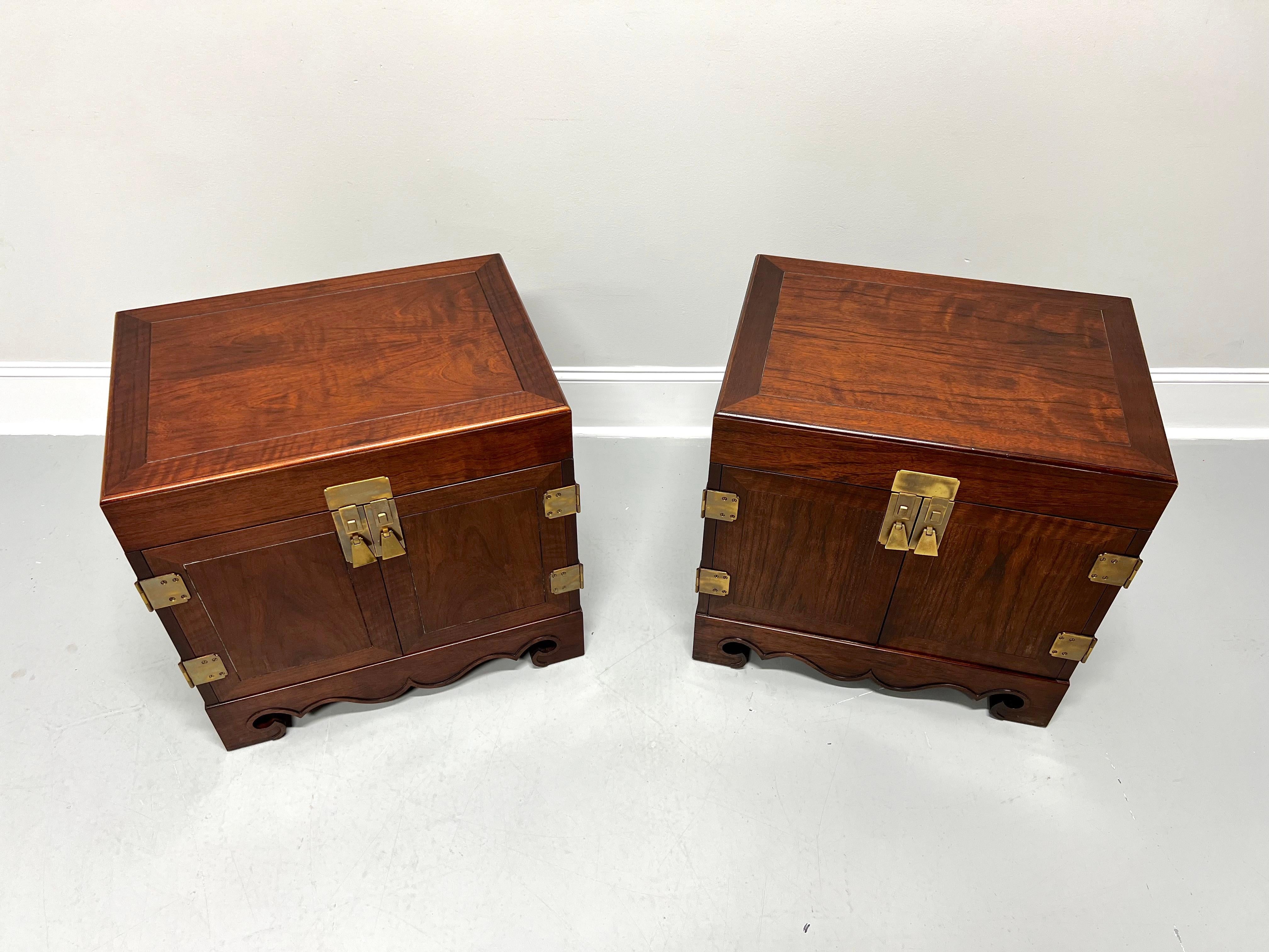 A pair of Asian inspired nightstands designed by Michael Taylor for Baker Furniture. Mahogany with banded bevel edge top, decorative brass hardware, brass side handles, carved apron, and carved bracket feet. Features two solid doors revealing