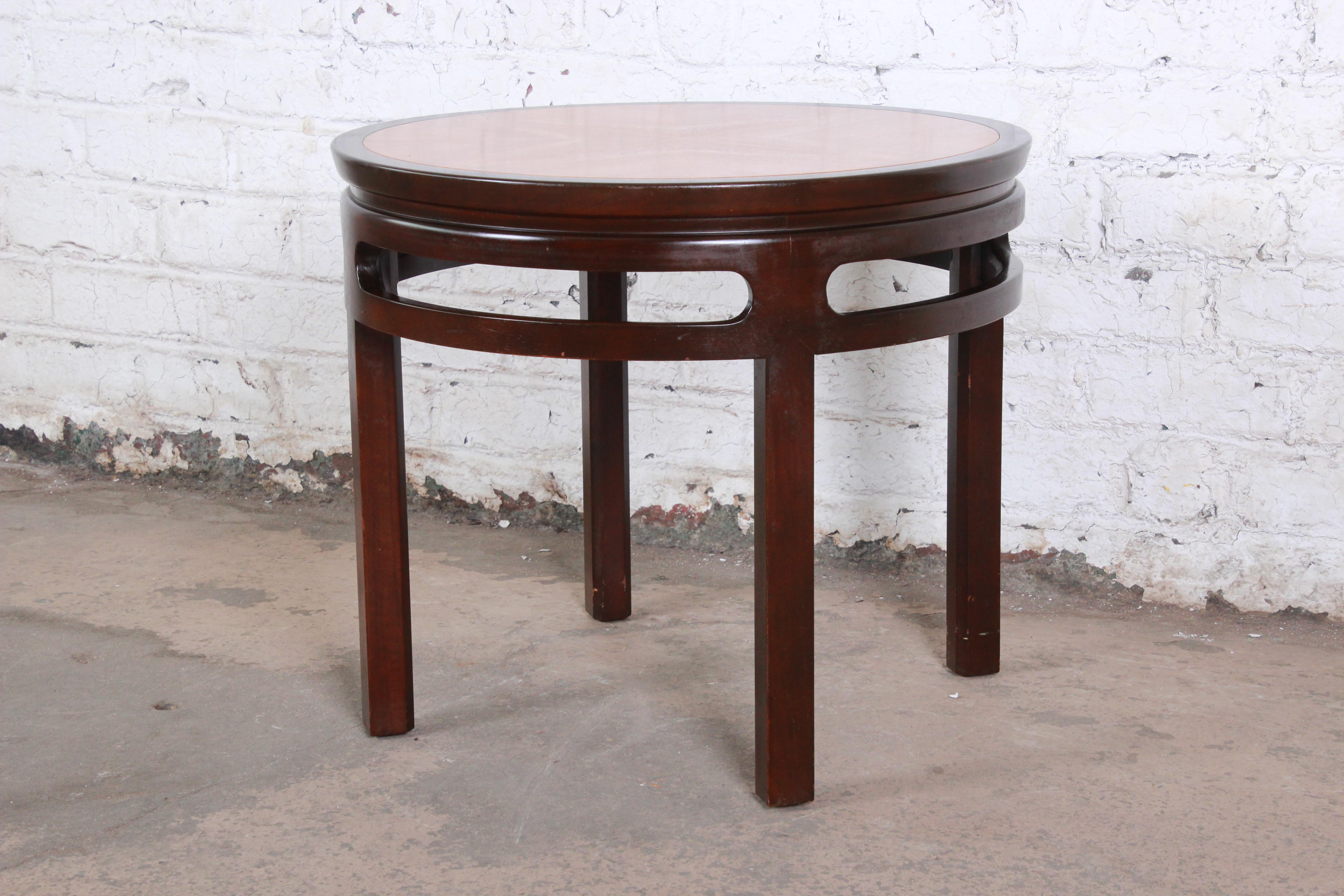 A gorgeous midcentury Hollywood Regency chinoiserie end table by Michael Taylor for Baker Furniture. The table features solid mahogany legs with a stunning book-matched teak top. It has a subtle Asian flair. The original Baker label is present. The