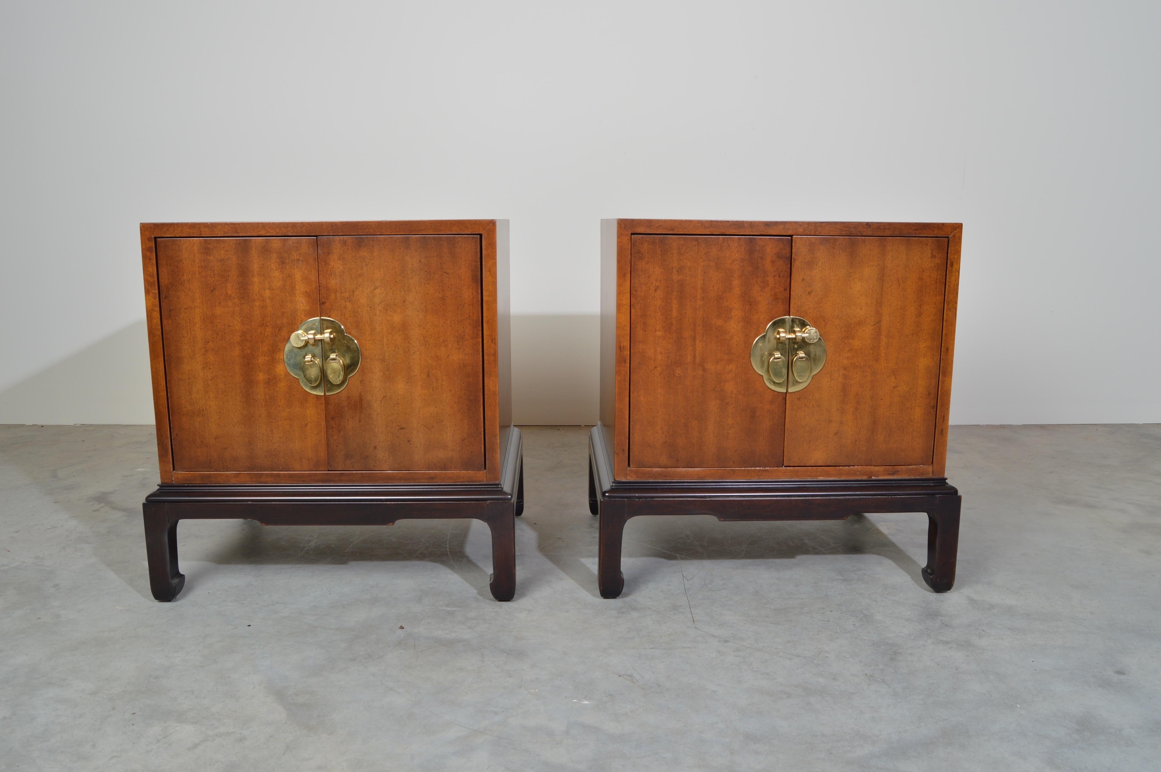 A pair of Ming dynasty influenced nightstands in walnut designed by Michael Taylor for Henredon of Morganton, North Carolina, USA. Made circa 1980. Each cabinet features a center shelf behind double doors with brass hardware and slide through brass