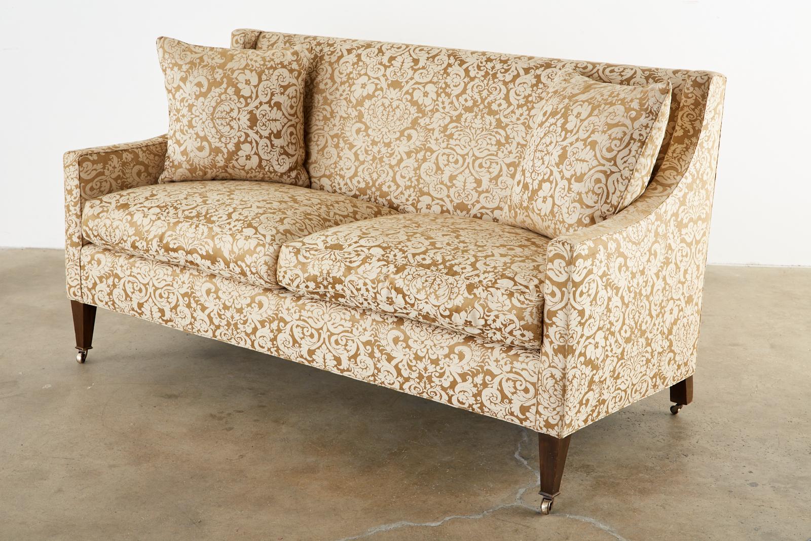 Stylish upholstered modern sofa settee featuring a Fortuny glicine style floral damask fabric by Michael Taylor. The modern settee has a hardwood frame with gracefully curved arms and a flat back. Supported by tapered legs ending with casters. The