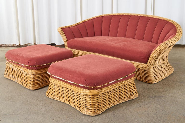 Distinctive woven rattan sofa and two matching ottomans made in the manner and style of Michael Taylor. The large sofa features a graceful waisted form with dramatic flared arms having a thick braided border. The inside has been upholstered with a